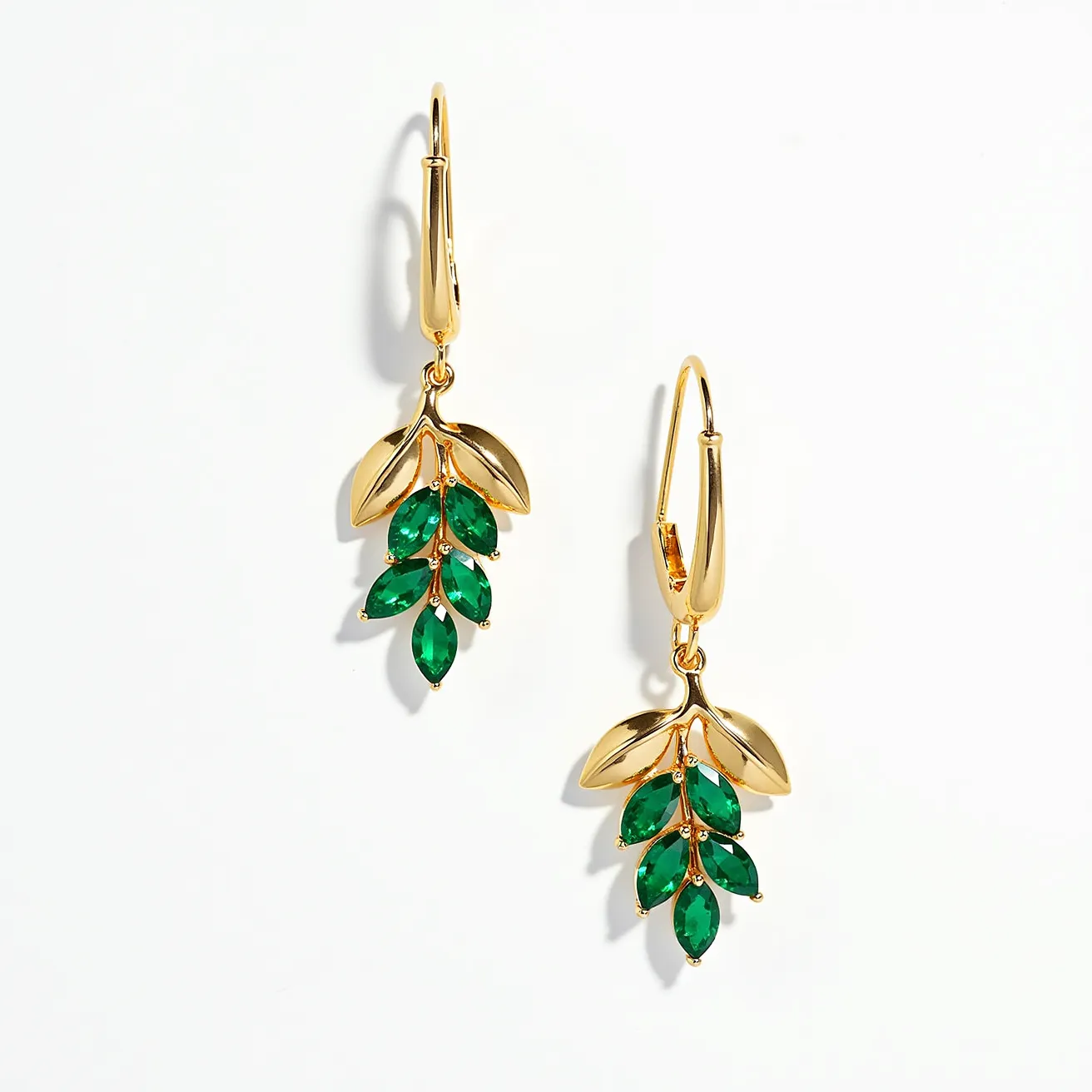 These drop earrings feature a graceful design composed of a gold-toned metal, shaped into delicate leaves that cascade elegantly. Each earring is adorned with vibrant green gemstones, cut in a marquise shape, which are artfully set in place to resemble leaves on a branch. The gems are securely mounted, enhancing the organic theme of the earrings. The earrings are attached via lever-back clasps, ensuring both security and comfort when worn. The harmonious combination of the gold and green creates a striking and natural aesthetic.