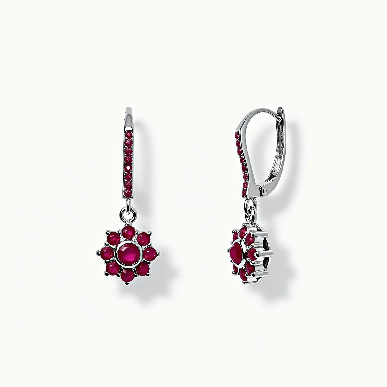 These drop earring features a striking floral design with vivid red gemstones set in a silver-toned metal. The central gemstone is round cut, surrounded by smaller, similarly cut stones arranged in a circular pattern, creating a flower-like appearance. These stones are securely held in place by a prong setting, enhancing their visibility and brilliance. The attachment is a lever-back clasp, adorned with additional small red stones, providing both security and style. The metal's polished finish complements the rich color of the gems, adding elegance to the overall design.