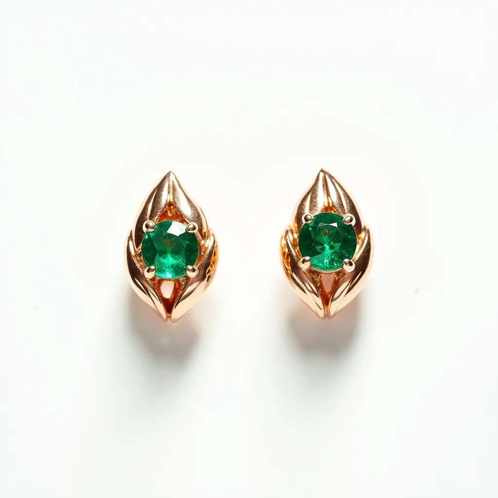 These emerald earrings feature a central, round-cut emerald gemstone nestled within a gold setting. The rich green hue of the emerald is striking and pairs elegantly with the warm tones of the gold, creating a luxurious appearance. Each earring is designed in a stylized leaf motif with the metalwork, which complements the natural beauty of the emeralds. The clasps or attachments, while not fully visible, suggest a secure and subtle mechanism that ensures comfort and stability when worn.