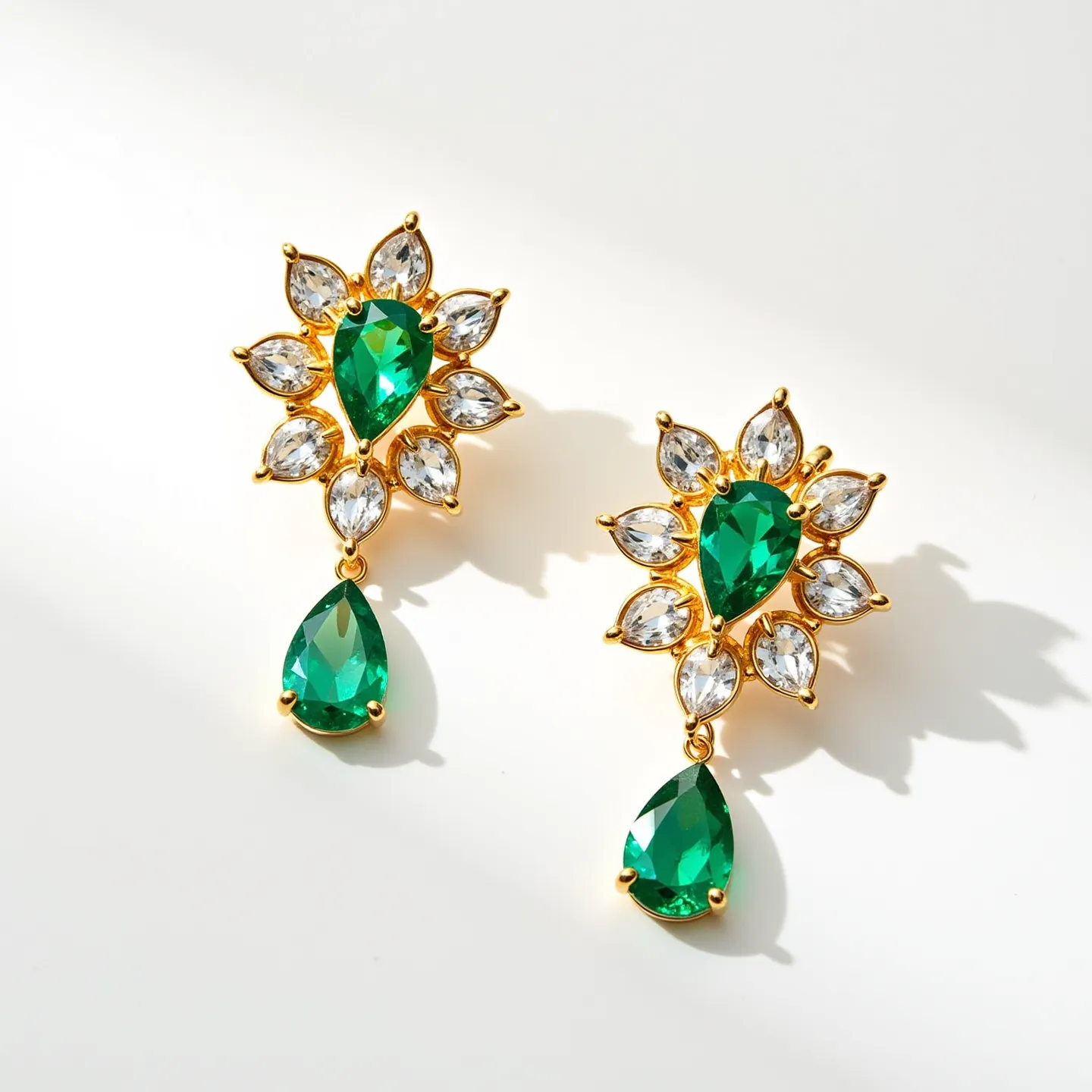 These emerald earrings feature a stunning array of gems and craftsmanship. The central design is highlighted by a large, pear-shaped emerald gemstone, skillfully cut to enhance its rich, vibrant hue. Surrounding the emerald are clear, marquise-cut stones, likely diamonds or high-quality crystals, arranged in a starburst pattern, adding a brilliant contrast and enhancing the overall elegance of the piece. Each stone is securely set in a gold-toned metal, adding a luxurious touch and ensuring durability. The earrings showcase a dangling emerald of the same pear shape, providing dynamic movement. The attachment is likely a post-back clasp, commonly used to ensure a secure and comfortable fit when worn.