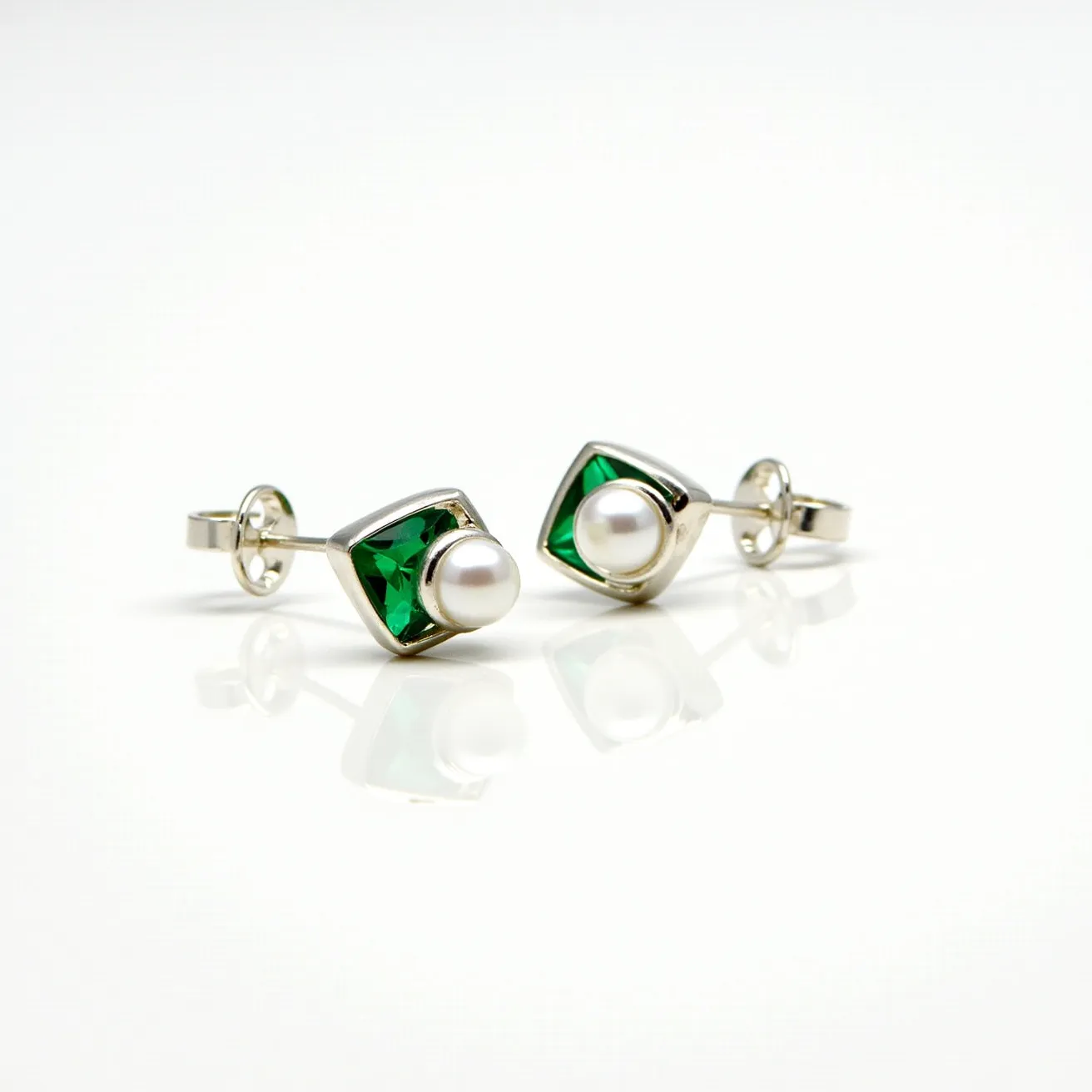 These emerald earrings feature a striking design with square-cut green stones, likely emeralds, set in a sleek metal, possibly silver or white gold. Each earring is adorned with a central pearl, adding a touch of elegance and contrast to the vivid green hue of the stones. The stones are securely housed in a bezel setting, which ensures their stability and highlights their color. The earrings utilize a standard post and butterfly clasp, providing a secure and comfortable fit for the wearer. The combination of emeralds and pearls creates a harmonious blend of classic and contemporary elements in this jewelry piece.