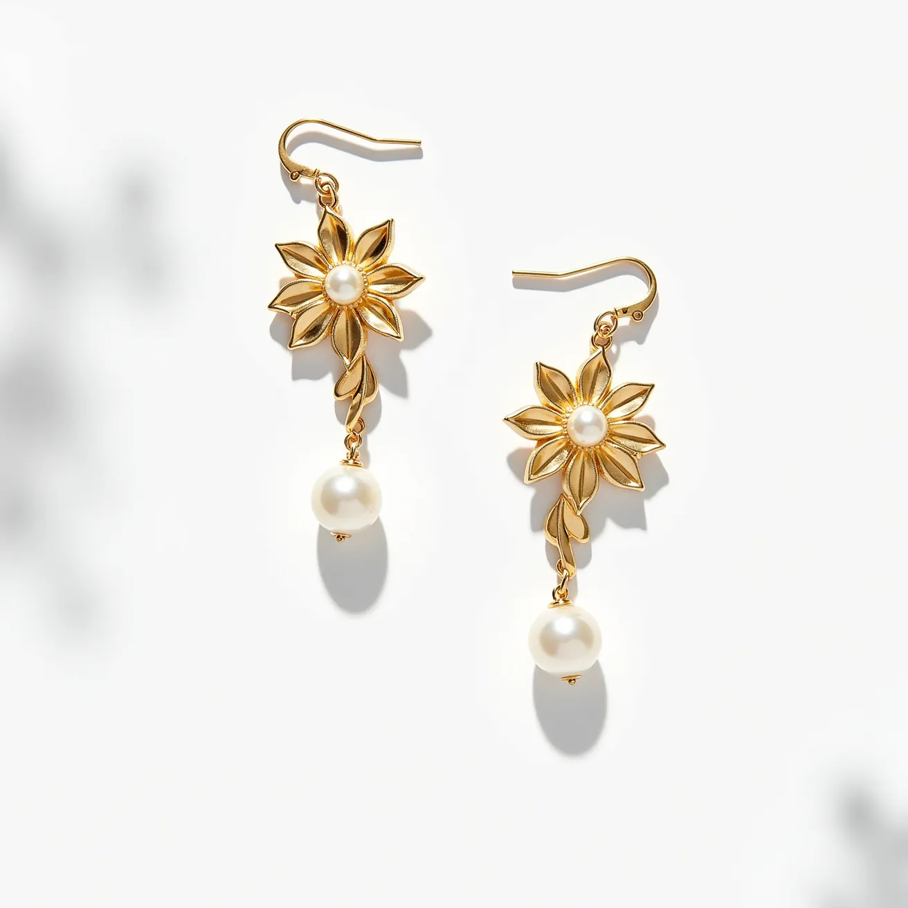 These floral earrings feature an elegant design with gold-toned metal petals arranged in a flower shape. At the center of the flower, there is a round pearl that serves as a focal point, enhancing the elegant appearance. The earrings also include a single, dangling pearl that hangs from the flower, adding to their sophisticated charm. The pearls likely imitate traditional freshwater or cultured pearls. The earrings are attached using a standard hook clasp, making them easy to wear and secure. The combination of the gold-toned metal and pearls creates a classic and timeless look.