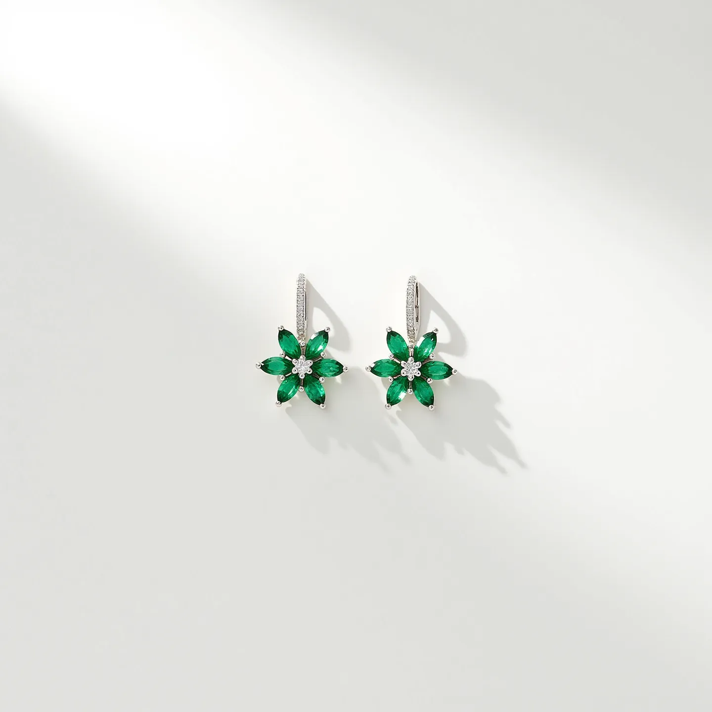 These flower earrings feature a delicate and elegant design with a floral motif. Each earring is adorned with six marquise-cut green stones, likely emeralds, arranged to form the petals of the flower. In the center, there is a round-cut white stone, possibly a diamond or cubic zirconia, serving as the focal point of the flower. The petals are set in a prong setting, allowing the stones to catch and reflect light beautifully. The earrings are crafted from a metal that appears to be white gold or platinum, adding to their sophisticated allure. For attachment, they have a latch-back clasp, ensuring secure wear while maintaining a seamless and polished appearance.