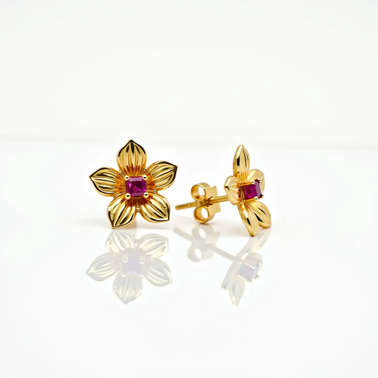 These flower earrings display a charming floral design crafted from a gold-toned metal that forms delicate, layered petals. Each earring is adorned at its center with a square-cut purple gem, securely held in place by a prong setting, which adds a touch of elegance and color. The earrings are equipped with a classic post and butterfly clutch back, ensuring a secure and comfortable fit when worn. The overall aesthetic combines the refined beauty of the gold finish with the vibrant hue of the central stones, creating a striking accessory suitable for various occasions.