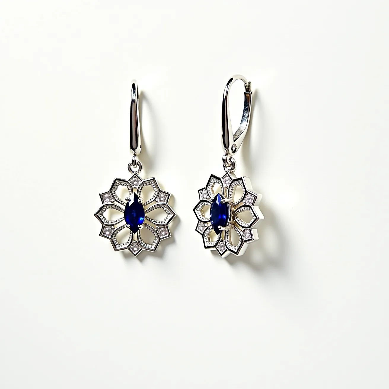 These flower earrings feature a striking design with a prominent flower motif. The earrings are crafted from a silver-toned metal, giving them a sleek and polished appearance. At the center of each earring, a marquise-cut deep blue gemstone is set in a secure prong setting, serving as the focal point of the floral design. The petals surrounding the gemstone have an intricate openwork pattern, bordered with small round clear stones that add a touch of sparkle. These earrings are attached to lever-back clasps, ensuring they are easy to wear and secure.