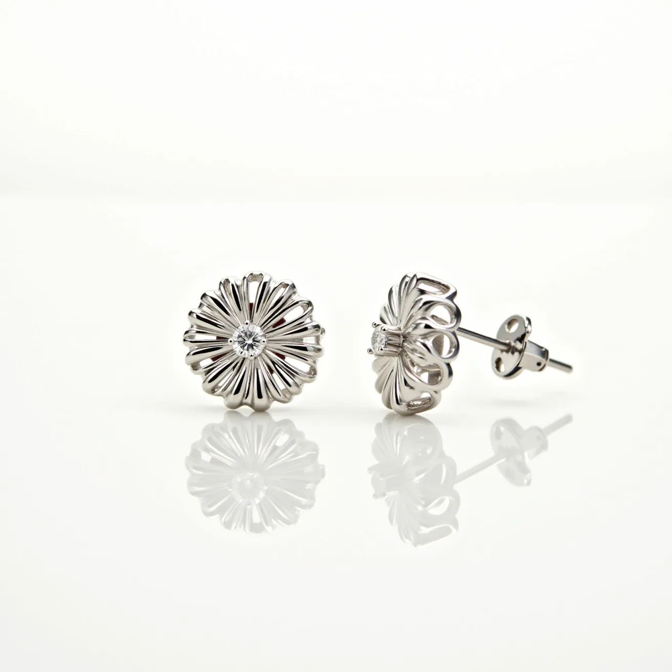 These flower earrings feature a detailed floral design crafted from a shiny metallic material, likely silver or white gold. Each earring is adorned with a single round-cut gem at the center, possibly a diamond, which is secured in a prong setting that complements the overall delicate design of the petals. The earrings are equipped with a post and butterfly clutch back attachment, ensuring a secure fit when worn. The intricate craftsmanship and choice of materials create an elegant and timeless style.