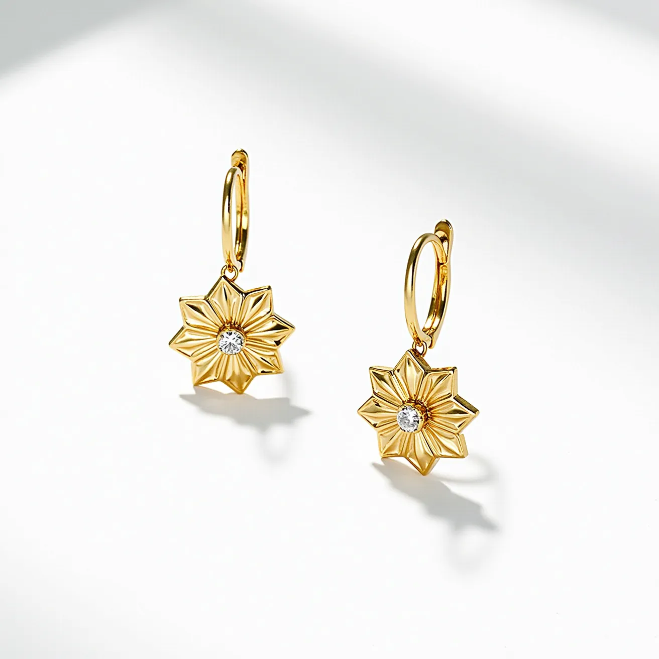 These flower earrings are crafted from polished gold-tone metal, shaped into a delicate floral design. At the center of each earring is a round-cut gemstone, likely a diamond or a diamond simulant, set securely into the floral motif, enhancing the piece's elegance and sparkle. The earrings are attached to a small hoop with a hinged clasp, providing a secure and stylish way to wear them. The overall design emphasizes both sophistication and feminine charm, ideal for adding a touch of elegance to any outfit.