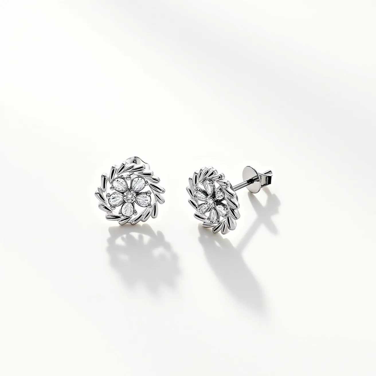 These floral stud earrings are crafted from a shiny silver-colored metal, likely sterling silver or white gold, showcasing a detailed floral design. The center of each earring features a cluster of round-cut and marquise-cut gemstones, possibly diamonds, that create a sparkling floral motif. These stones are set in a prong setting, enhancing their brilliance and allowing light to pass through. The earrings are designed with a post and butterfly clasp attachment, ensuring a secure fit when worn. The intricate design and elegant materials make these earrings an exquisite accessory.