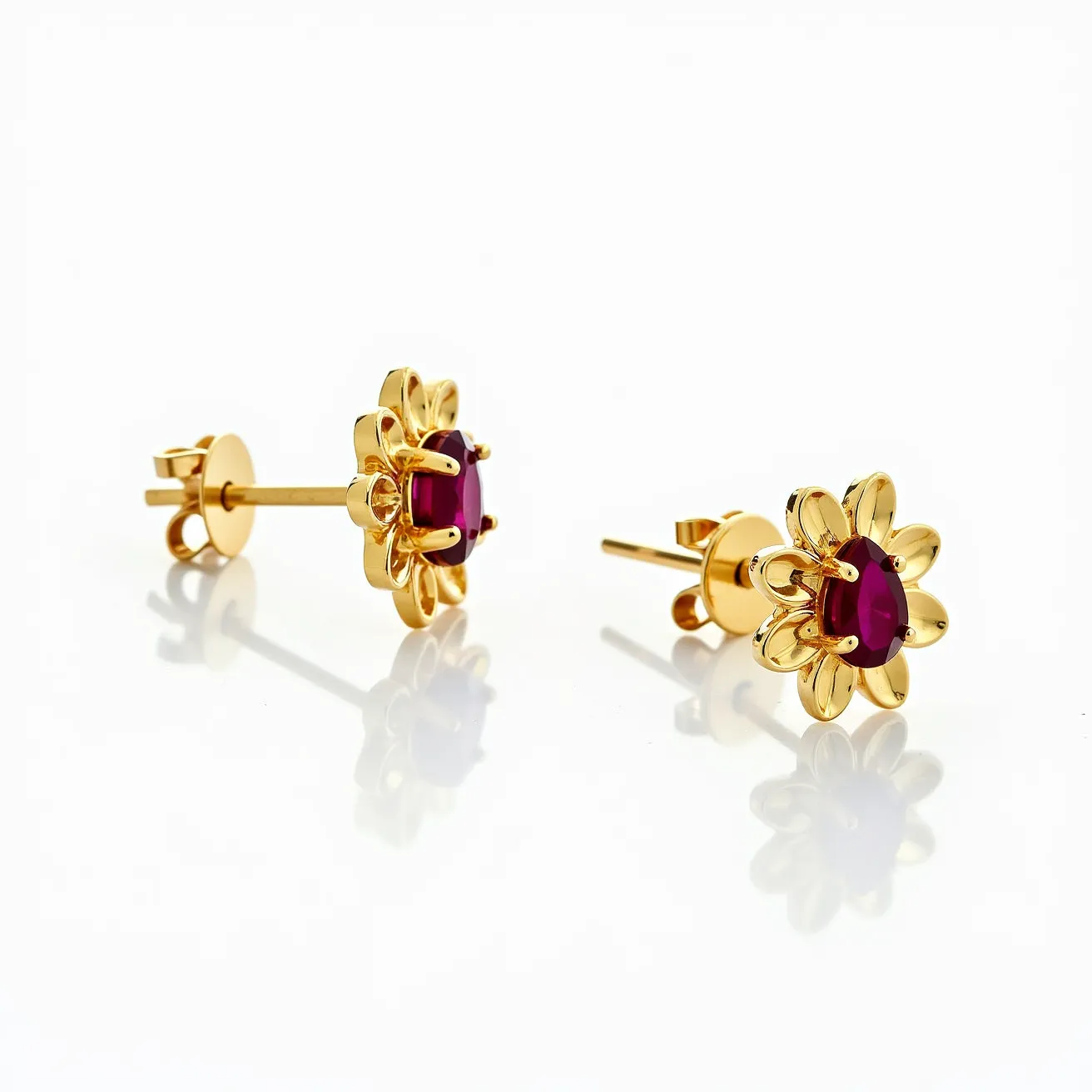 These floral stud earrings feature a sophisticated design, crafted in a polished gold that forms the petals of the flower. At the center of each earring is an oval-cut ruby, securely held in place by a prong setting, which enhances the vibrant red hue of the gemstones. The attachment comprises a straightforward post and butterfly clasp, ensuring a secure and comfortable fit for the wearer. These earrings elegantly blend the allure of precious stones with the timeless beauty of gold, making them a striking accessory for any occasion.