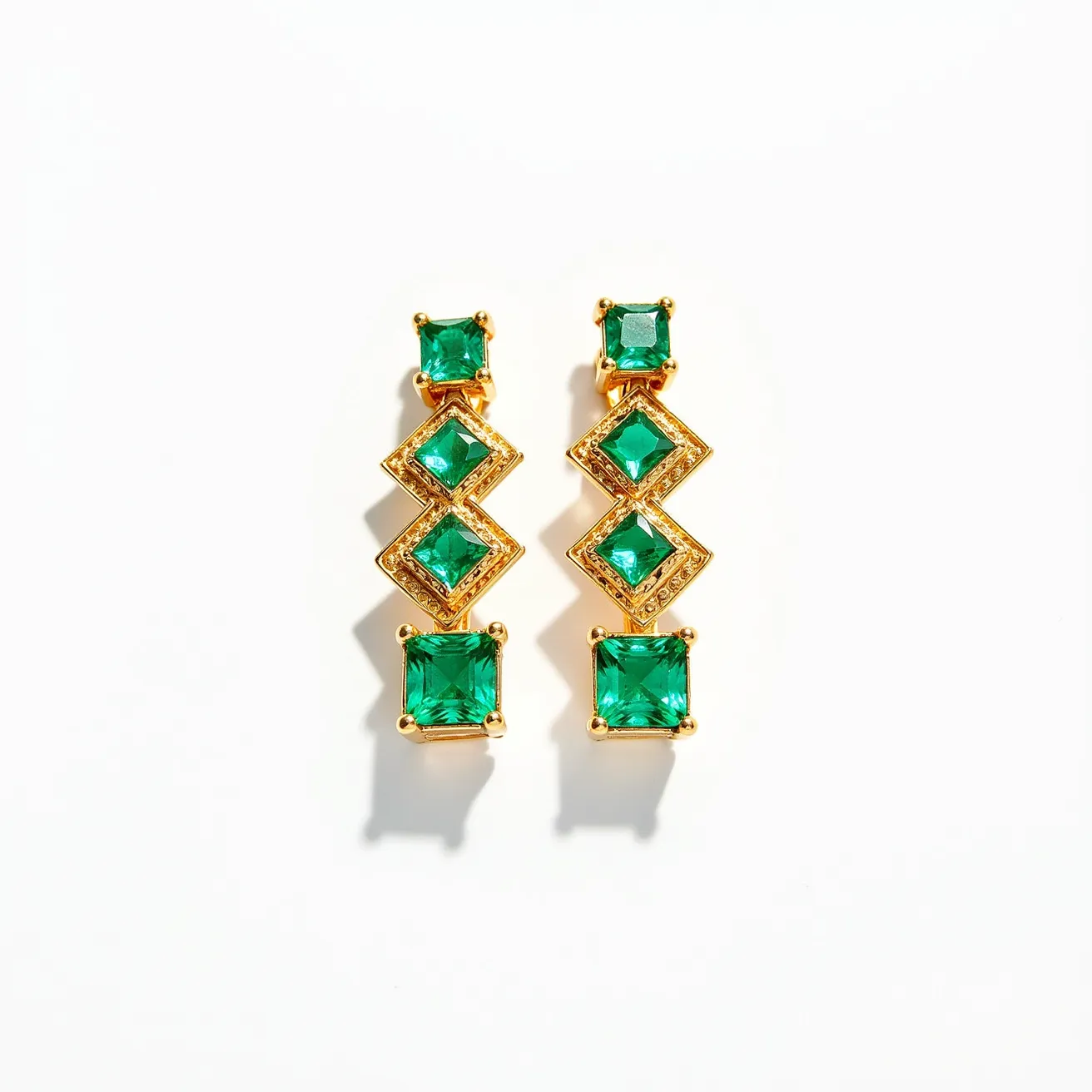 These gemstone earrings feature a series of vibrant green stones, likely emeralds, set in a gold-toned metal. The stones are mainly square-cut, with some creatively arranged in a diamond orientation to create visual interest. Each earring consists of four stones graduated in size, starting with a smaller square-cut stone at the top, followed by two slightly larger ones set in a diamond shape, and culminating in a larger square-cut stone at the bottom. The settings appear to be prong settings, securely holding each gem in place, while the earrings themselves likely hang from a post or hook style attachment, allowing them to dangle elegantly.