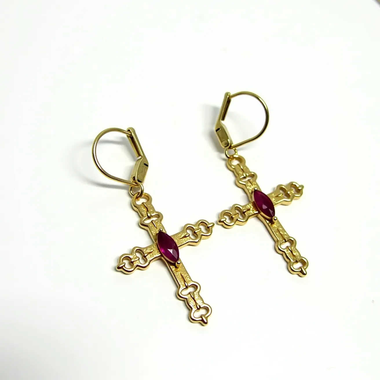 These gold cross earrings feature intricately designed crosses crafted from a rich, yellow gold material. Each cross is adorned with a single marquise-cut gemstone, likely a ruby or garnet, set at the center, adding a touch of vivid red to the design. The stones are securely held in a bezel setting, enhancing their prominence against the metal backdrop. These earrings use lever-back clasps, providing a secure and comfortable fit while also complementing the ornate style of the crosses. The delicate metalwork and vibrant gems combine to create a striking and elegant accessory.