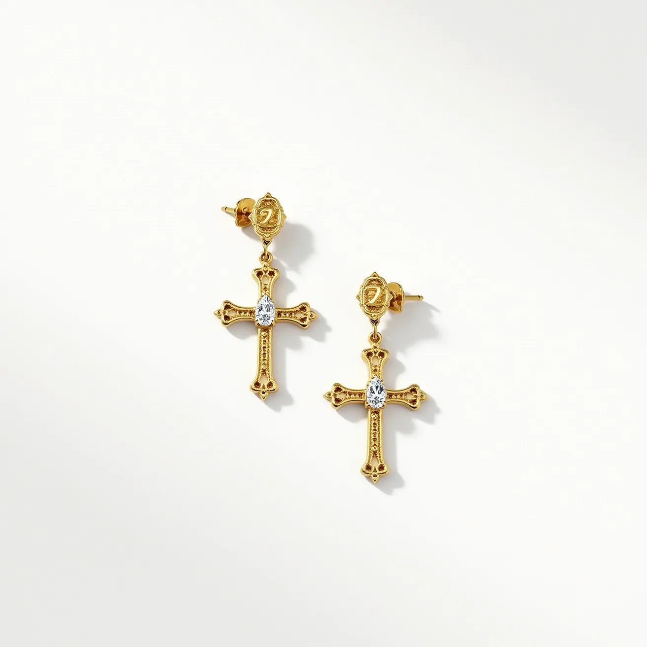 These gold cross earrings feature a beautiful, intricate design crafted from polished gold. At the center of each cross is an oval-shaped, clear gem, likely a diamond or cubic zirconia, set securely in a bezel setting that highlights its brilliance. The cross showcases detailed engravings and has a symmetrical pattern, which adds to its elegance. The earrings are attached with a traditional post and butterfly clasp, ensuring a secure fit while being stylish and suitable for various occasions.