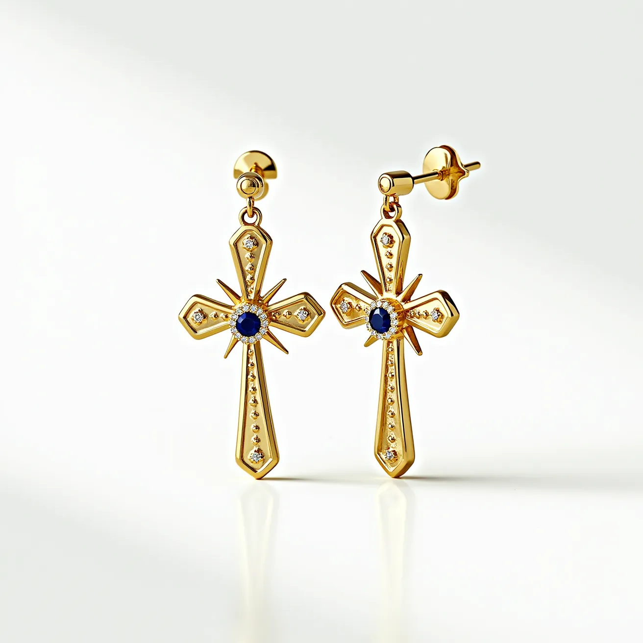 These gold cross earrings feature a polished metal structure with a central blue gemstone, likely a sapphire, cut in a round shape and set in the middle of each cross. Surrounding the central stone are smaller round diamonds, enhancing the design with a halo effect. The edges of the cross are adorned with additional smaller diamonds, each carefully set to add extra sparkle and complement the central gem. The earrings are attached using a post and butterfly back clasp, providing a secure fit. The combination of the rich gold and sparkling stones highlights an elegant and luxurious design.