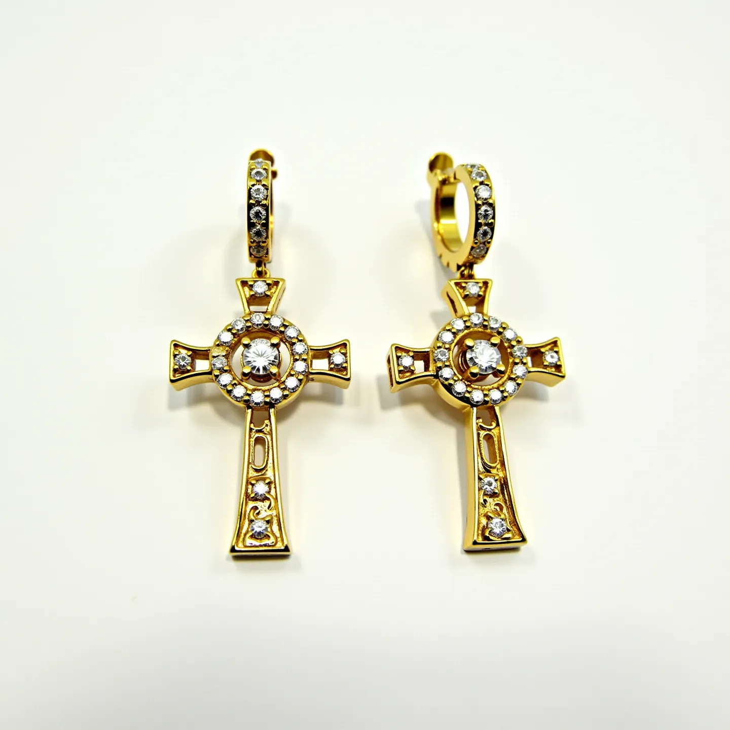 These gold cross earrings feature a striking design crafted from polished gold. Each earring showcases a prominent, round clear stone at the center of the cross, surrounded by a circle adorned with smaller clear stones, enhancing the overall sparkle. Additional stones embellish the ends of the cross and the length of the vertical bar, adding to the luxurious appearance. The earrings are attached to small hoops that are also encrusted with multiple clear stones, completing the elegant look. These earrings are designed with a hinged clasp mechanism, ensuring secure and comfortable wear.