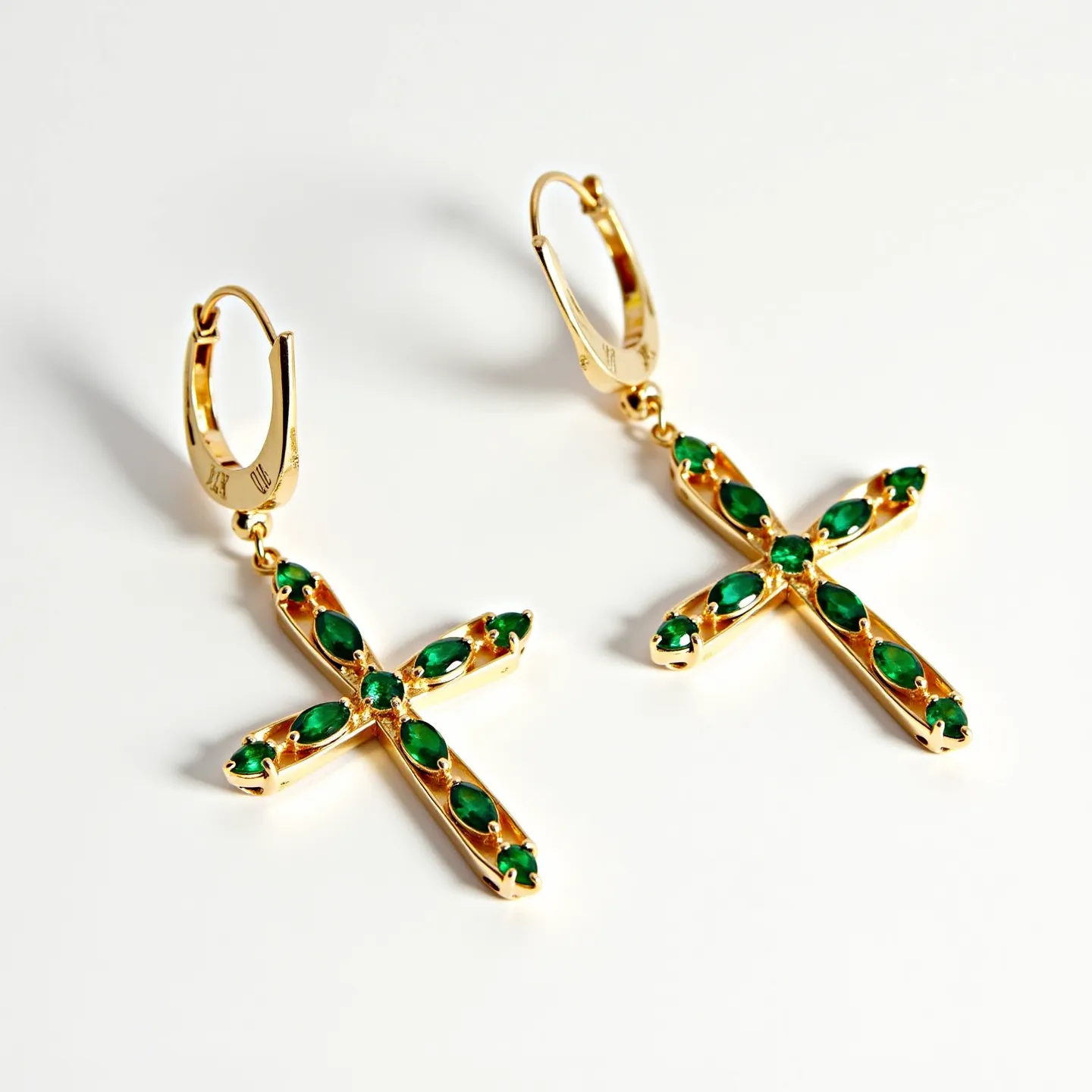 These gold cross earrings feature a sleek and polished gold setting, showcasing a series of vibrant green gemstones. The stones are likely emeralds, given their deep green color, and are cut in a combination of round and marquise shapes. These stones are set securely in a prong setting, which highlights their luminous quality. The crosses dangle from a small circular hoop, which serves as the attachment method, using a lever-back clasp for secure wearability.