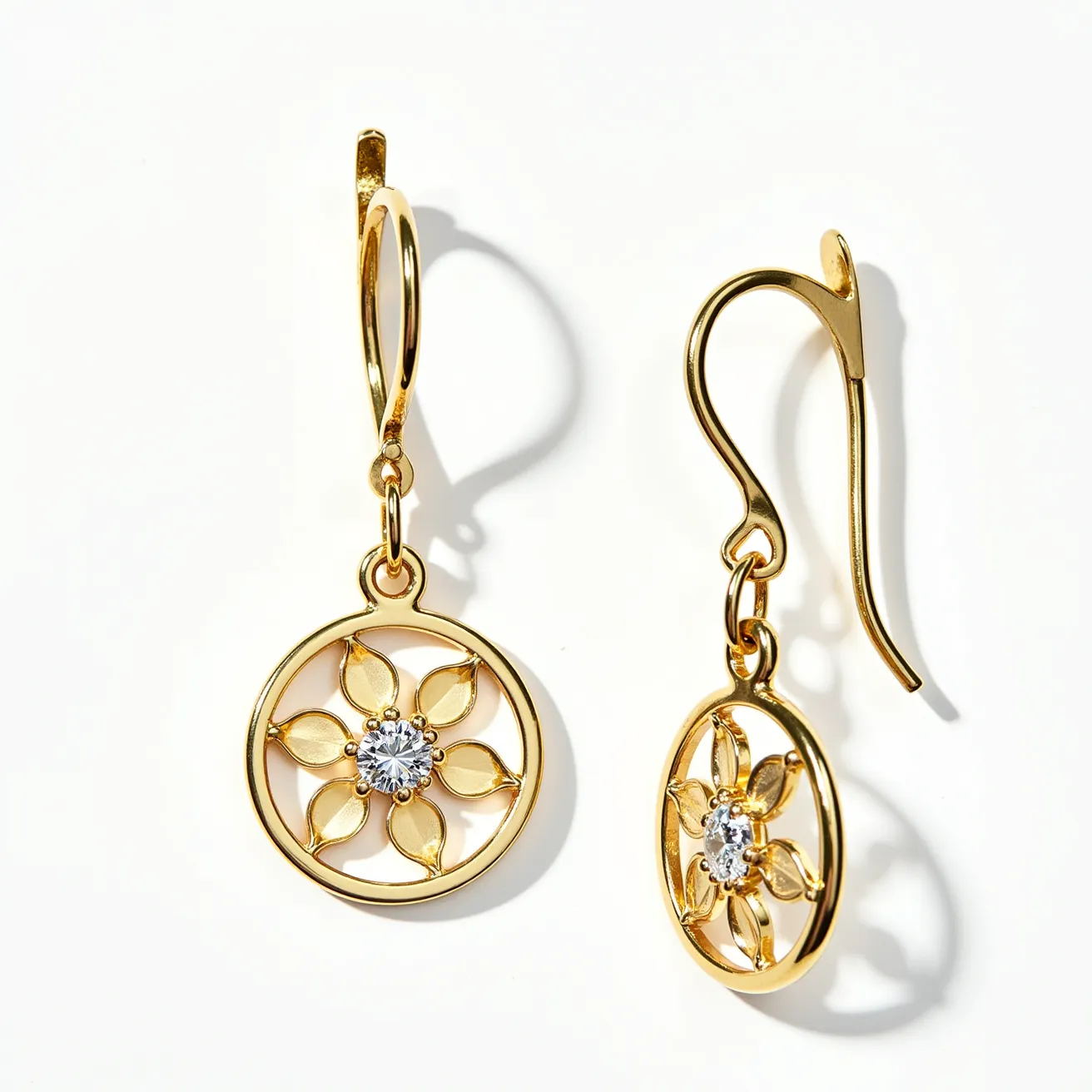 These gold dangle earrings feature an intricate circular design, expertly crafted from what appears to be a polished gold material. At the center of each earring, a faceted round-cut gemstone is set in a delicate prong setting, adding a touch of sparkle and elegance. The gemstones are surrounded by a floral pattern, with petal-like shapes radiating outward, enhancing the overall ornamental look. The earrings are equipped with hinged lever-back clasps, ensuring a secure and comfortable fit when worn.