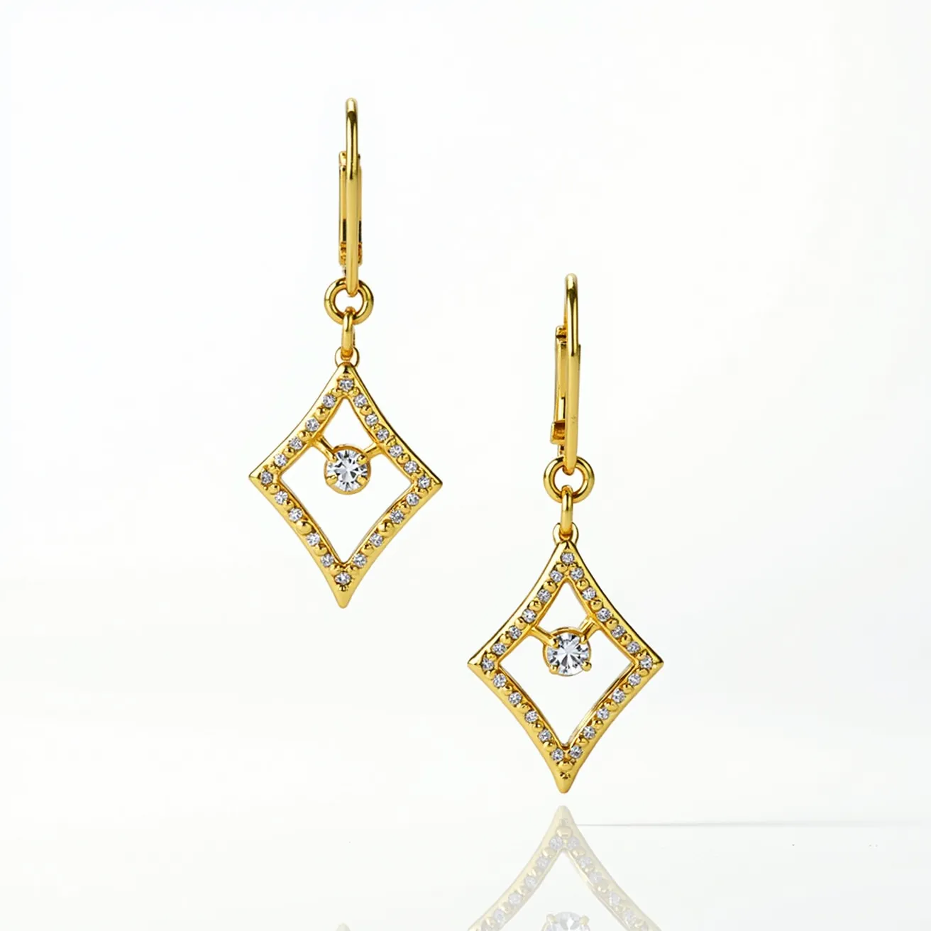 These gold dangle earrings feature a geometric diamond shape crafted from a gold metal framework. The outer edge of each earring is adorned with a series of small, evenly set round-cut clear stones, possibly diamonds, that add a touch of brilliance to the design. At the center of each geometric frame, a single, larger round-cut stone is suspended, likely incorporating a prong setting that enhances its visibility and sparkle. The earrings are attached to lever-back clasps, providing secure and comfortable wear. The elegant interplay of gold and clear stones makes these earrings a striking accessory for various occasions.