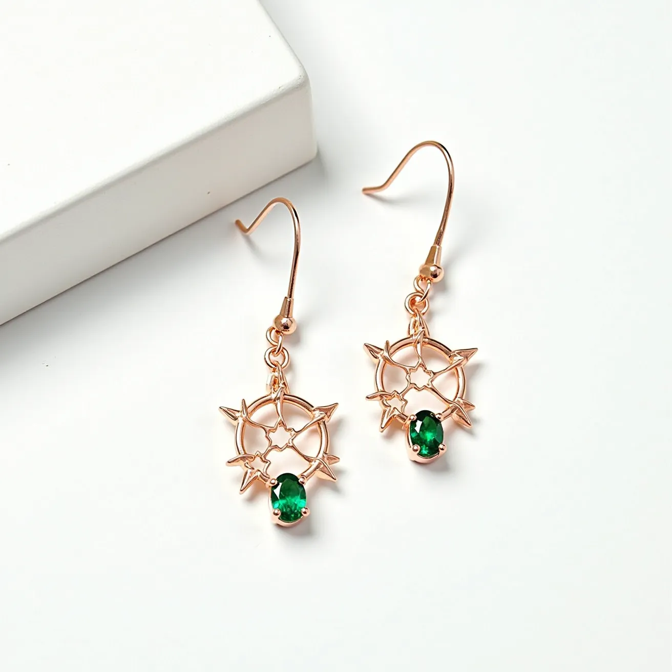 These gold drop earrings feature a delicate star-like design crafted from gold, highlighting an elegant openwork pattern. Each earring is adorned with a prominent oval-cut green gemstone, securely set in a prong setting at the base of the design. The earrings utilize a fish hook attachment, providing both simplicity and ease of wear. The combination of the gold framework and the vibrant green gemstones creates a striking contrast, adding a touch of sophistication to the overall design.