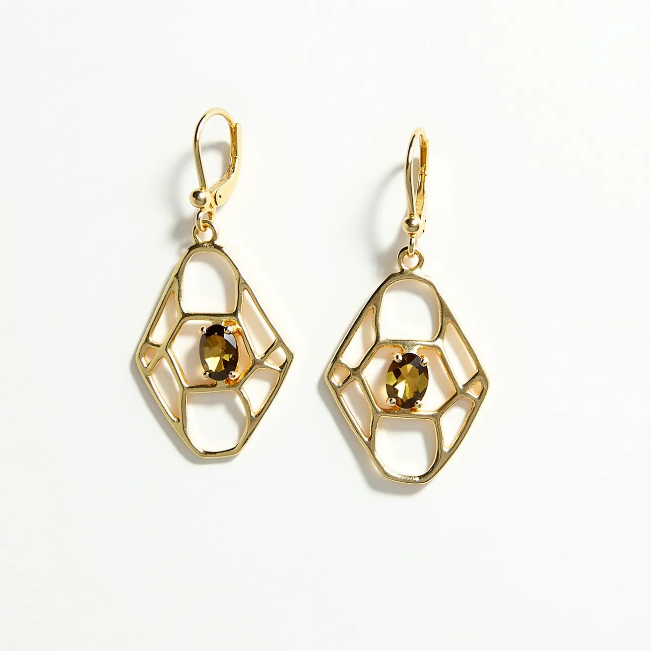 These gold drop earrings feature a stylish geometric design with an open lattice framework, crafted from gold. Each earring showcases a central, oval-cut gemstone set with prongs, adding a touch of elegance and sparkle to the overall look. The gemstones have a rich, amber hue, enhancing their warm appeal. The earrings are equipped with leverback clasps, ensuring a secure and comfortable fit for the wearer.