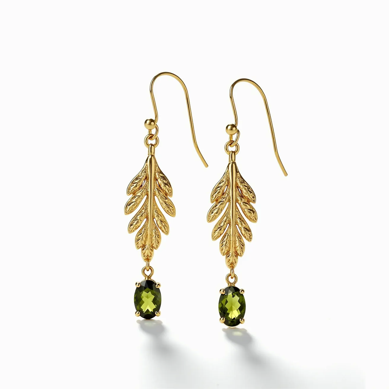 These gold drop earrings feature an elegant leaf motif crafted from gold, providing a natural and sophisticated design. Dangling from the base of each leaf is an oval-cut green gemstone, which appears to be held securely in a prong setting, adding a touch of vibrant color to the piece. The earrings are equipped with a classic fishhook clasp, allowing for ease of wear and movement. The combination of the textured gold leaves and the sparkling green stones creates a striking contrast, making these earrings a stylish and eye-catching accessory.