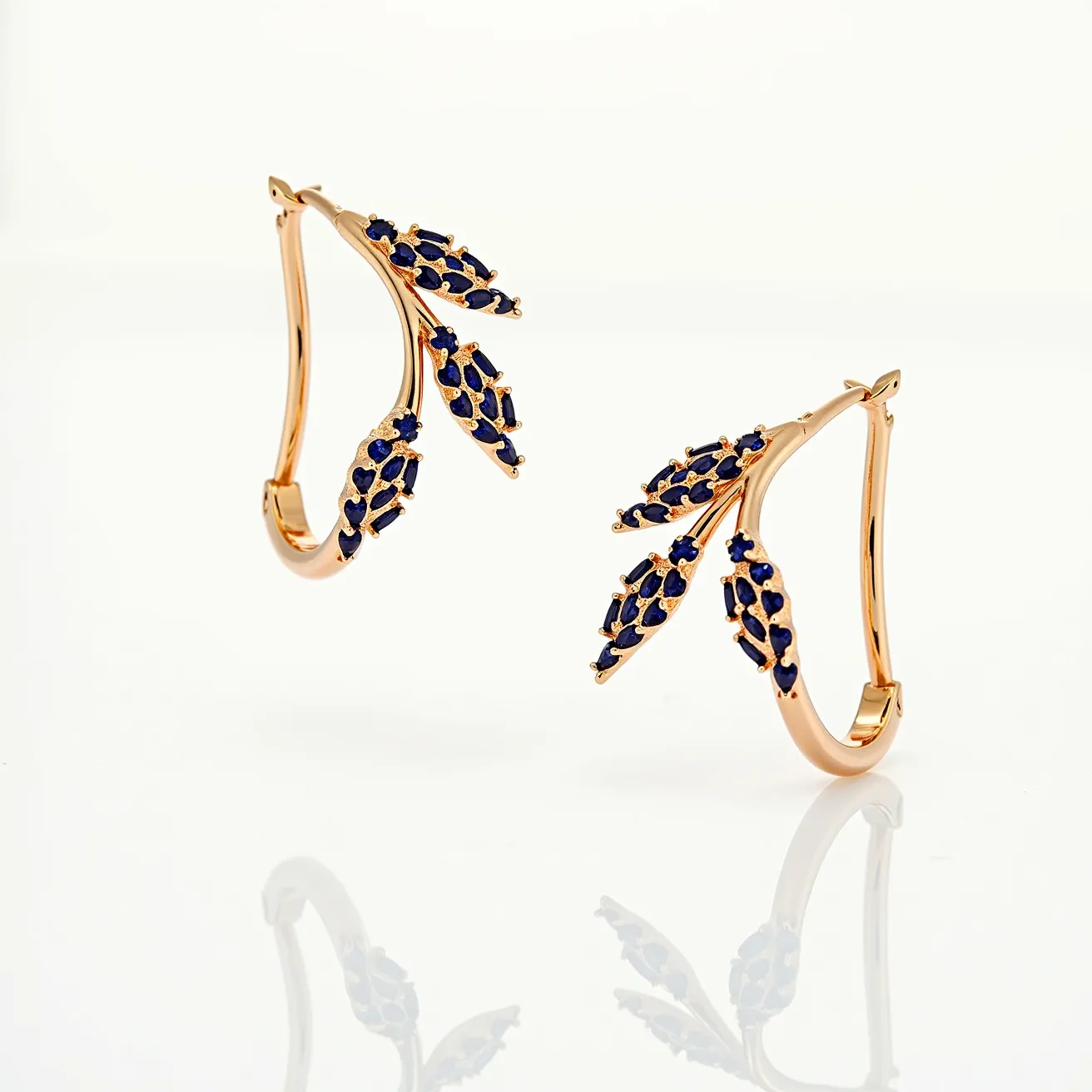 These gold earrings feature a delicate design, crafted from gold and adorned with deep blue gemstones. The stones are small and are artistically arranged in clusters, suggesting a prong setting that enhances their visibility and sparkle. The earrings are designed in the form of elegant branches or petals, with each segment studded with gemstones, adding a touch of sophistication. They secure with a latch-back clasp, ensuring they stay comfortably and securely in place when worn. The overall design is both stylish and timeless, making these earrings a versatile addition to any jewelry collection.