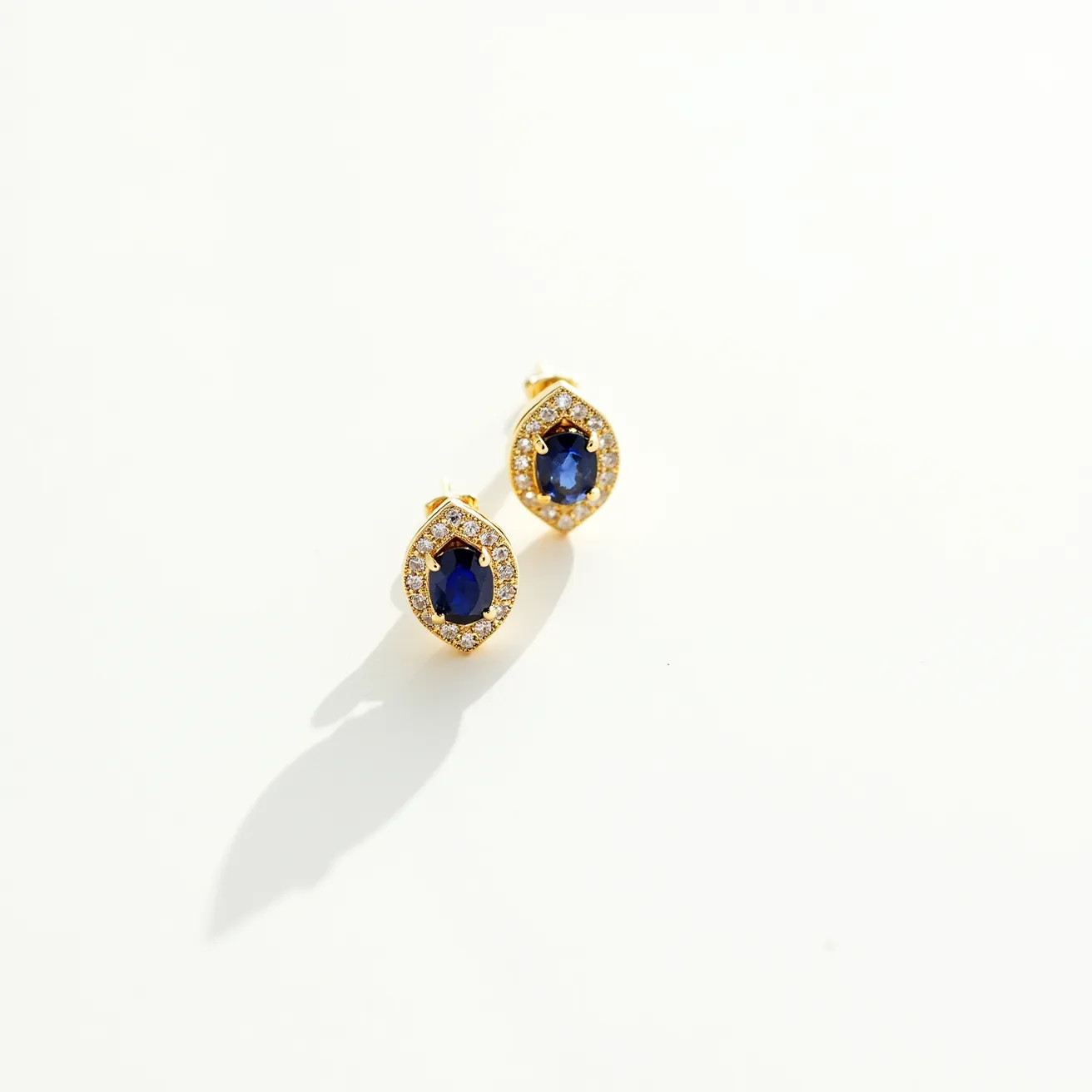 These gold earrings feature an elegant design with an oval-shaped sapphire at the center, surrounded by a halo of smaller diamonds. The deep blue sapphire is set in a prong setting, which ensures both security and maximum light exposure to the stone. The diamonds are also held in prong settings, emphasizing the brilliance and adding a touch of sparkle around the primary gemstone. The gold used in the earrings has a rich, warm hue, complementing the vibrant color of the sapphire. The earrings appear to be secured with a post and butterfly clasp, providing ease of wear and a secure fit.