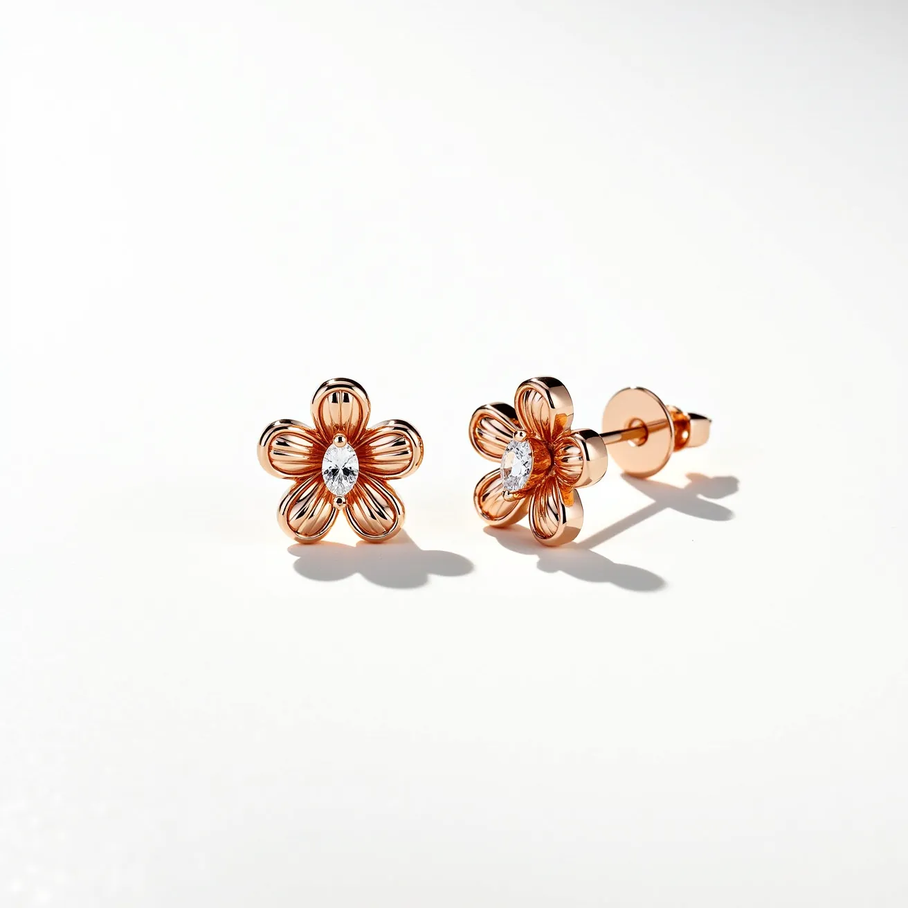 These gold flower earrings are crafted from a polished gold material forming an elegant floral design. Each earring features a single marquise-cut gem at the center, likely a diamond or a similar clear gemstone, set delicately to enhance the shimmering effect. The petals are beautifully shaped with a textured finish, adding depth to the floral motif. The earrings are secured with a classic push-back clasp, ensuring a comfortable and stable fit.