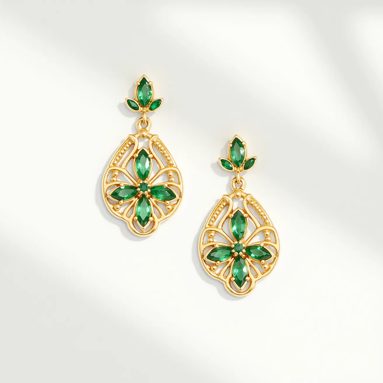 These gold flower earrings feature an intricate floral design crafted from gold, showcasing their elegant structure. The earrings are adorned with green marquise-cut stones, delicately set to form the petals of the flower, with a smaller, round green stone at each center, highlighting the overall floral motif. These stones are securely set in a bezel setting, ensuring both security and style. The earrings have a drop design, connecting the flower motif to a smaller, coordinating green stone that sits at the ear lobe. They are attached with a post-back clasp, providing ease of wear and a secure fit.