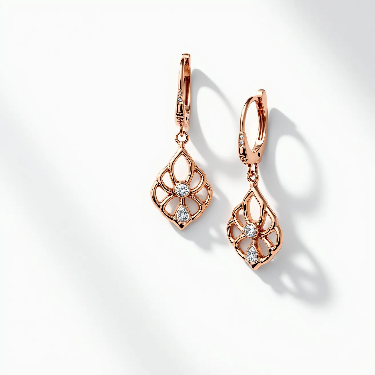 These gold flower earrings feature an elegant design crafted from rose gold metal. Each earring showcases a symmetrical floral motif with open petal patterns, intricately formed. At the center and toward the bottom of each flower are brilliant-cut gemstones, likely diamonds, set within the gold structure. The stones are securely held in place with a bezel setting, adding an extra touch of sophistication. The earrings are equipped with secure lever-back clasps, ensuring they stay comfortably in place when worn.