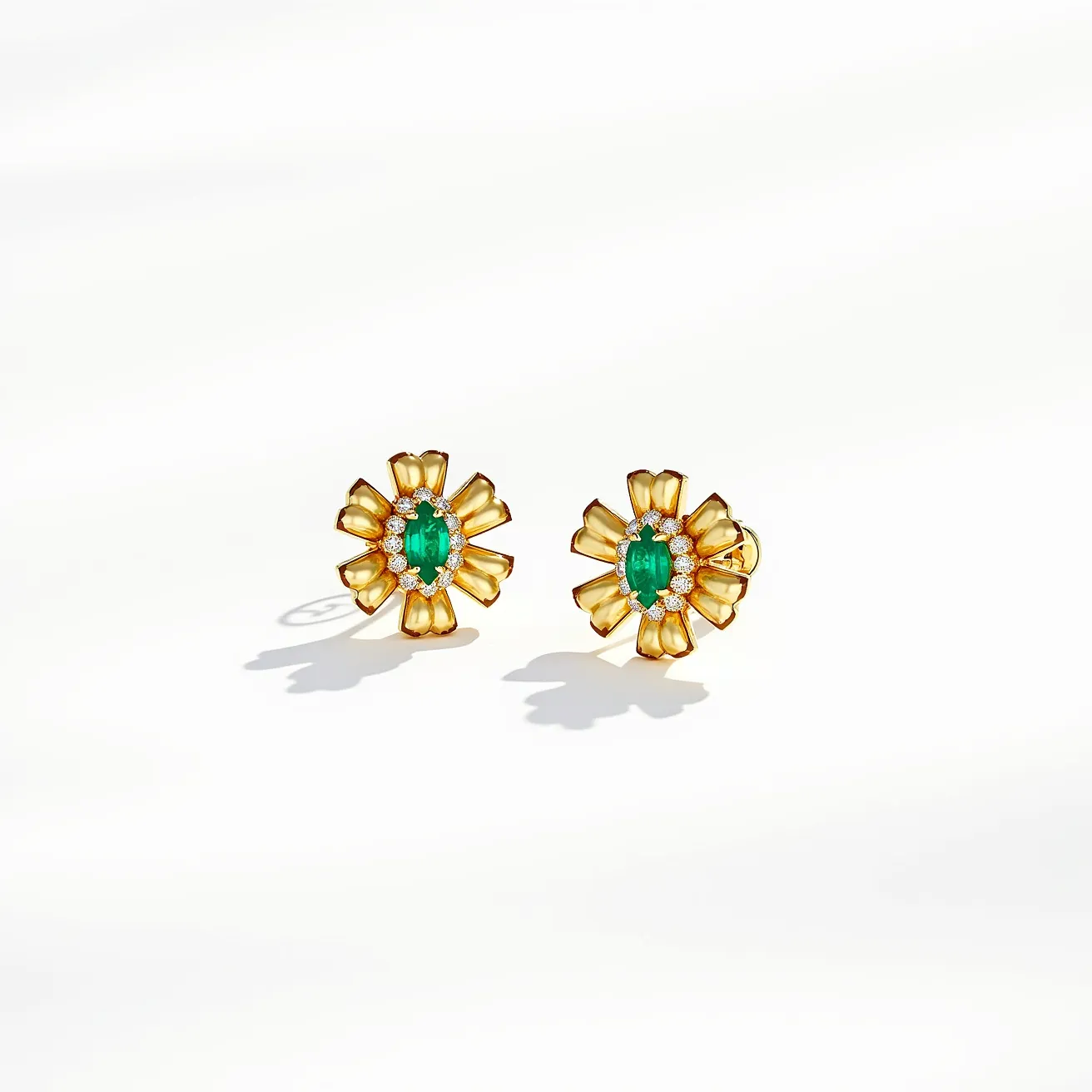 These gold flower earrings feature a striking design with a prominent central green gemstone, likely an oval-cut emerald, nestled securely in a prong setting. Encircling the emerald are several small, round-cut diamonds arranged in a sparkling halo. The petals of the flower are crafted from polished gold, with a lustrous finish that enhances the luxurious aesthetic. The earrings are fitted with a post back clasp for secure and comfortable wear.