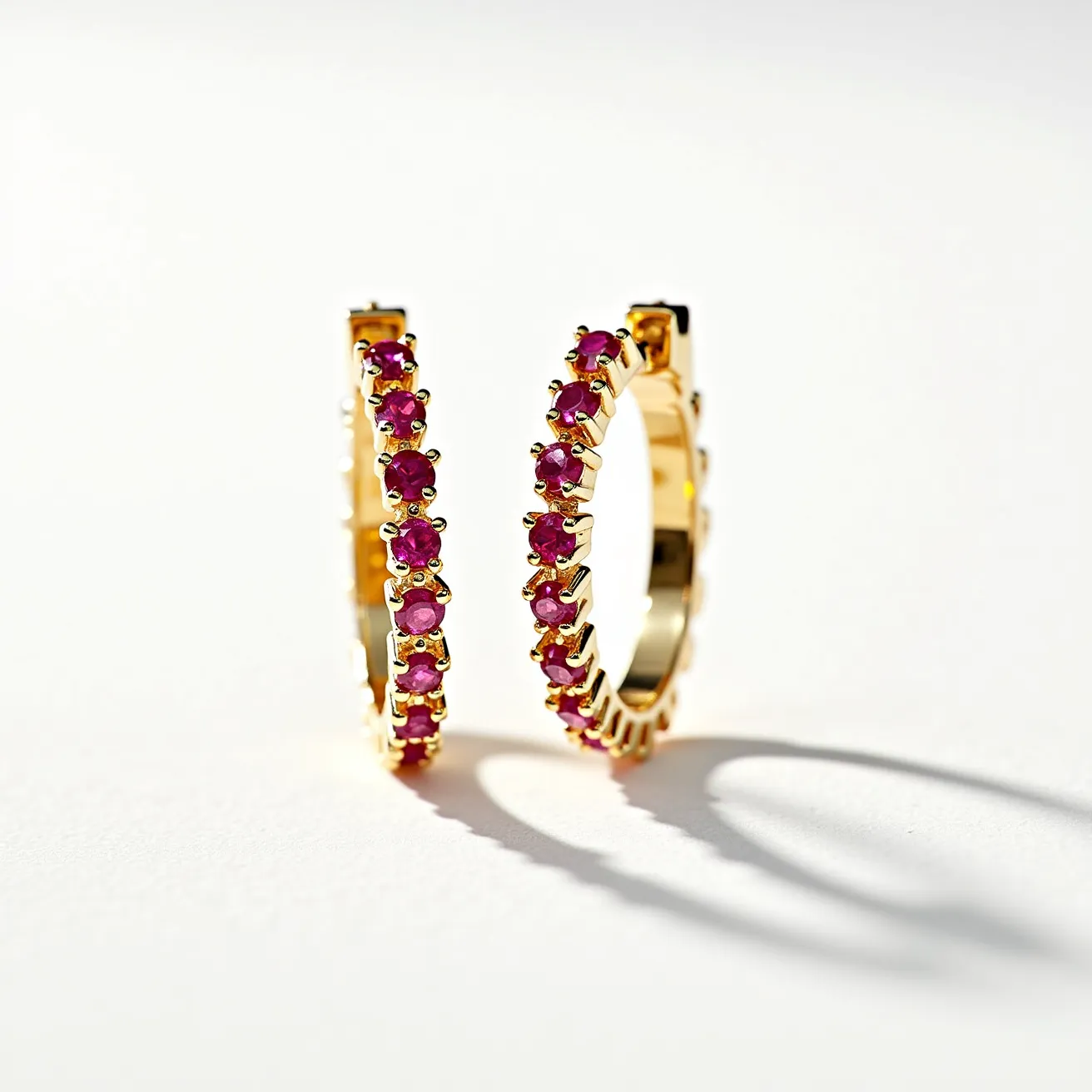 These gold hoop earrings showcase a stunning arrangement of red gemstones, likely rubies, that are round-cut and prong-set along the entire circumference of the hoops. The gold metal serves as an elegant and classic base, enhancing the vibrant hue of the stones. Each gem is securely held with multiple prongs, adding a secure and refined finish to the design. The hoop mechanism appears to feature a hinge clasp, providing ease of wear while maintaining a seamless circular shape. The overall appearance is both timeless and sophisticated, making these earrings a versatile accessory for various occasions.