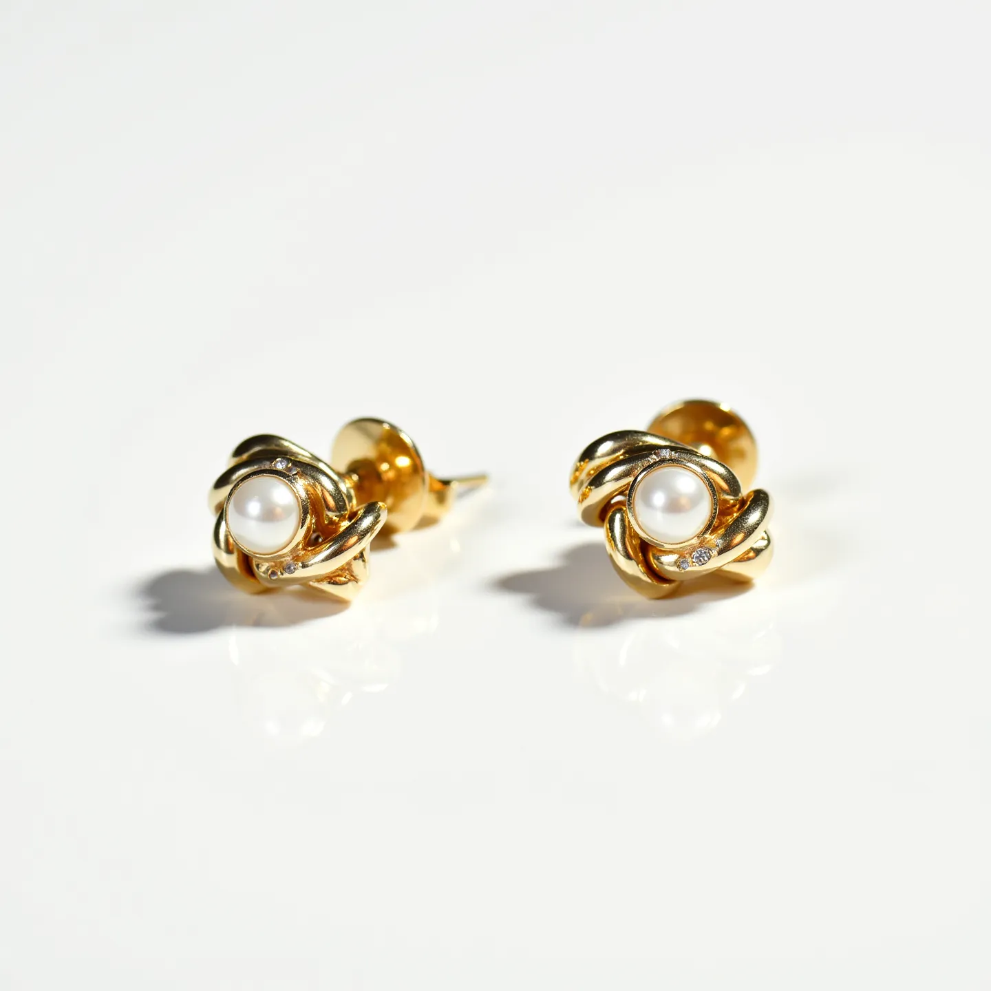 These gold knot earrings feature a central pearl, elegantly set within a twisted gold design that forms a knot shape. The gold appears to be polished and may be made from a standard gold alloy given its sheen and texture. Each earring includes small diamond accents, likely round-cut, positioned subtly within the gold twists to enhance their sparkle and elegance. The earrings use a typical push-back clasp for attachment, ensuring secure and comfortable wear.