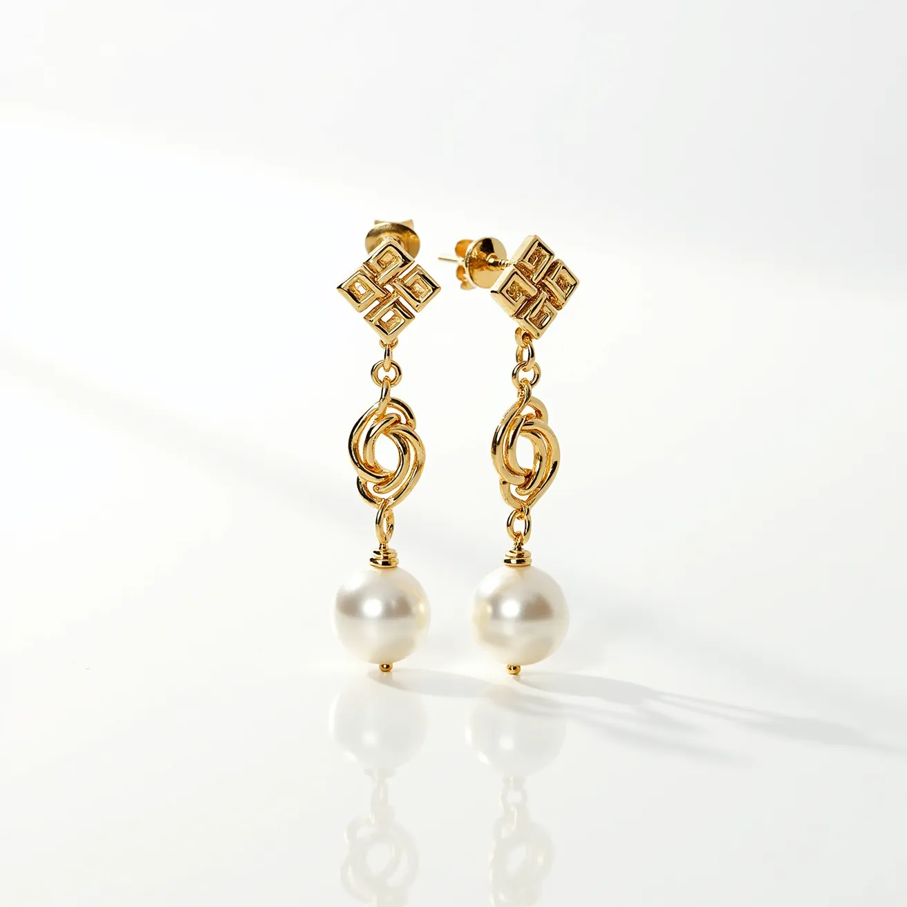 These gold knot earrings feature intricately designed knot motifs crafted from gold, showcasing a polished and luxurious finish. Suspended below the knots are lustrous, spherical pearls, adding a classic elegance to the design. The pearls are secured with a simple gold peg setting, allowing them to dangle gracefully. The earrings are attached via a post and butterfly clasp, ensuring a secure fit when worn.