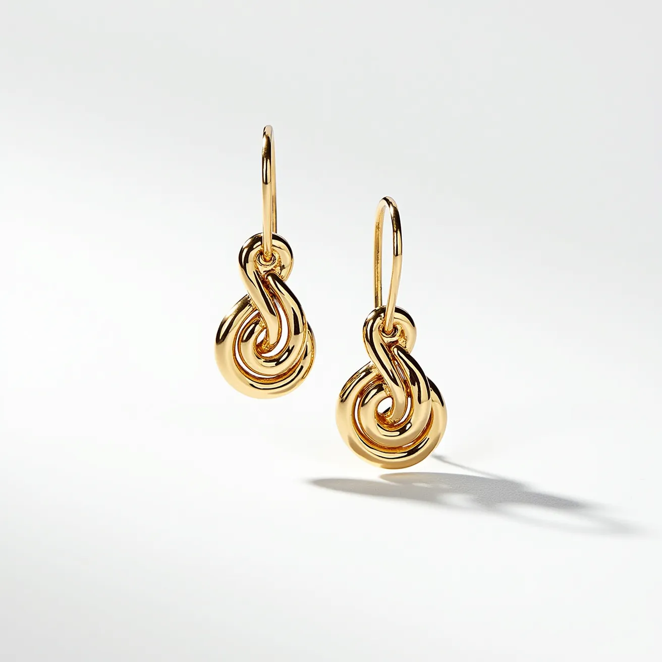 These gold knot earrings feature an intricate design of intertwined loops, expertly crafted from polished gold. These earrings exhibit a beautiful shine, showcasing the warmth and elegance typically associated with quality gold jewelry. The knots are suspended from a hook-style attachment, which allows for graceful movement and ease of wearing. The craftsmanship emphasizes a seamless blend of curves and contours, highlighting the artistry of the piece.