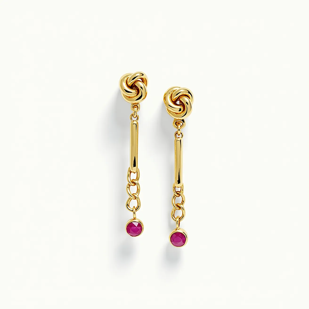 These gold knot earrings feature a beautifully intertwined design crafted from polished gold, creating an elegant and timeless appeal. The earrings are adorned with a vibrant red gemstone, possibly a ruby, which is round cut and bezel set at the end of a delicate chain. The design includes a post and push-back clasp, providing a secure attachment while maintaining the earrings' sophisticated look. The combination of the gold knot and the striking gemstone enhances their luxurious aesthetic.