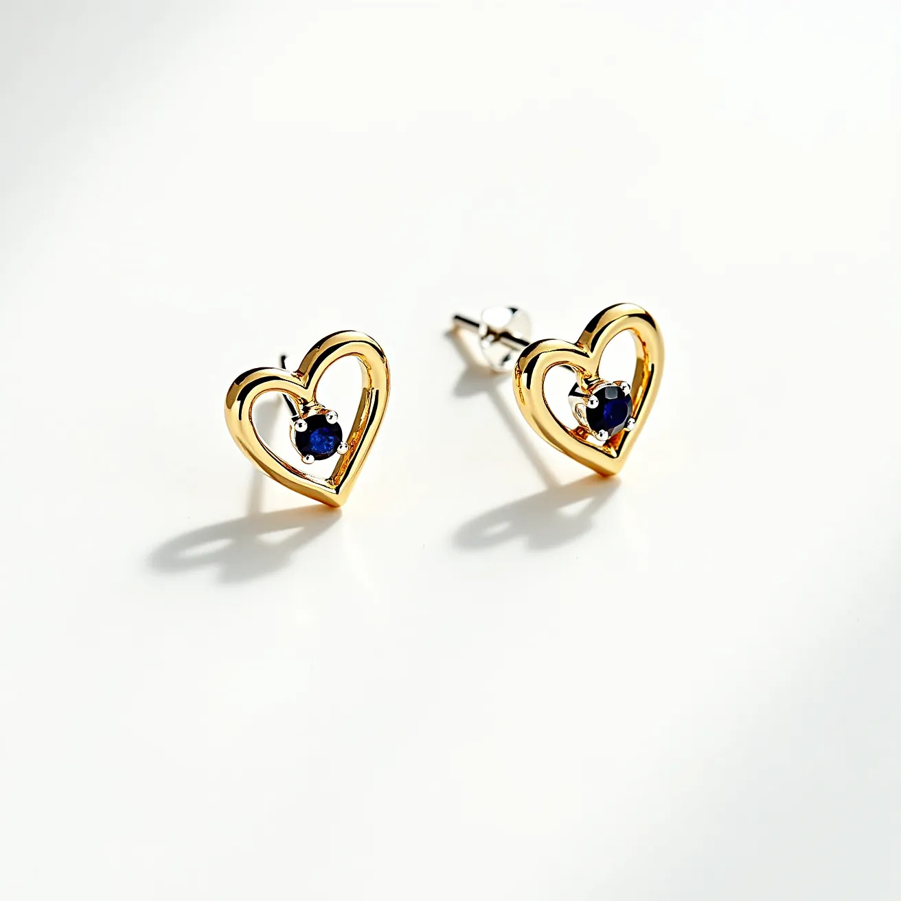 These gold stud earrings feature a heart-shaped design crafted from polished gold, providing a sleek and elegant look. At the center of each heart is a round, faceted sapphire gemstone set in a classic prong setting, adding a pop of deep blue color that complements the warm gold tone. The earrings are secured with a standard post and butterfly clutch back, ensuring a comfortable and secure fit on the earlobe. The combination of gold and sapphire creates a timeless and versatile piece of jewelry suitable for various occasions.