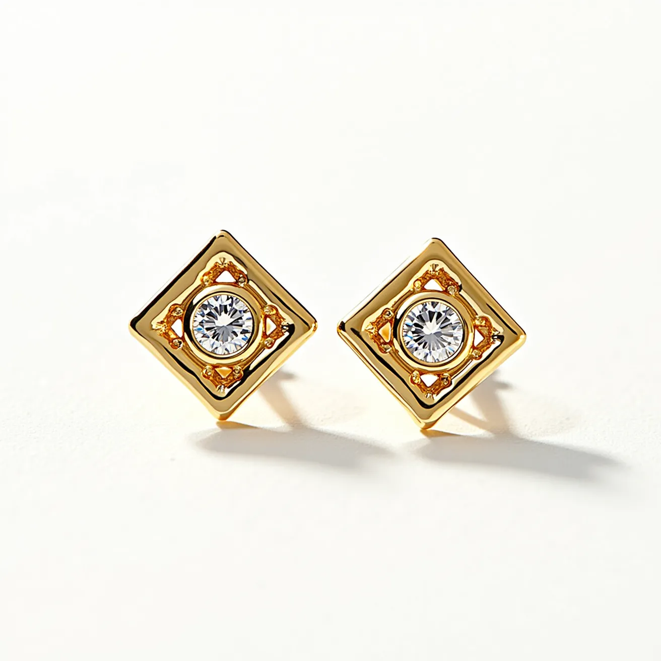 These gold stud earrings feature a square-shaped design, crafted from gold with a prominent central gemstone. Each earring is adorned with a round-cut stone, likely a clear or diamond-like gem, securely set at the center. The setting is elegantly enclosed with small ornate detailing around the stone, adding an intricate touch to the design. The earrings are fitted with a classic push-back post, ensuring a snug and secure fit when worn.