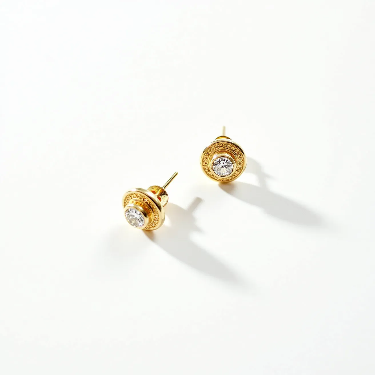 These gold stud earrings feature a central round-cut gemstone that is set within a detailed gold bezel setting, accented with intricate designs enhancing their elegance. The gold material gives the earrings a classic and luxurious appearance. Each earring is secured with a standard post and butterfly clasp, ensuring they stay comfortably in place when worn. The overall design combines traditional craftsmanship with a touch of sophistication, making them suitable for both everyday wear and special occasions.