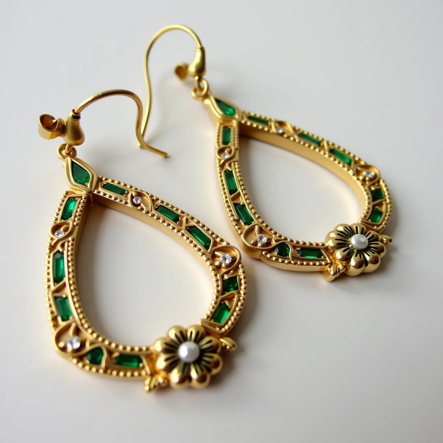 These gold teardrop earrings feature a stylish combination of green stones set into the frame, intricately bordered with detailed goldwork. Each earring is adorned with small, round, clear gemstones, possibly diamonds or cubic zirconia, set into a bezel setting that enhances their brilliance. The apex of the teardrop is decorated with a delicate floral motif, centered with a small, round white gem, contributing to the earrings' sophisticated design. The earrings are secured with a classic fishhook clasp, ensuring a secure fit while providing ease of wear.