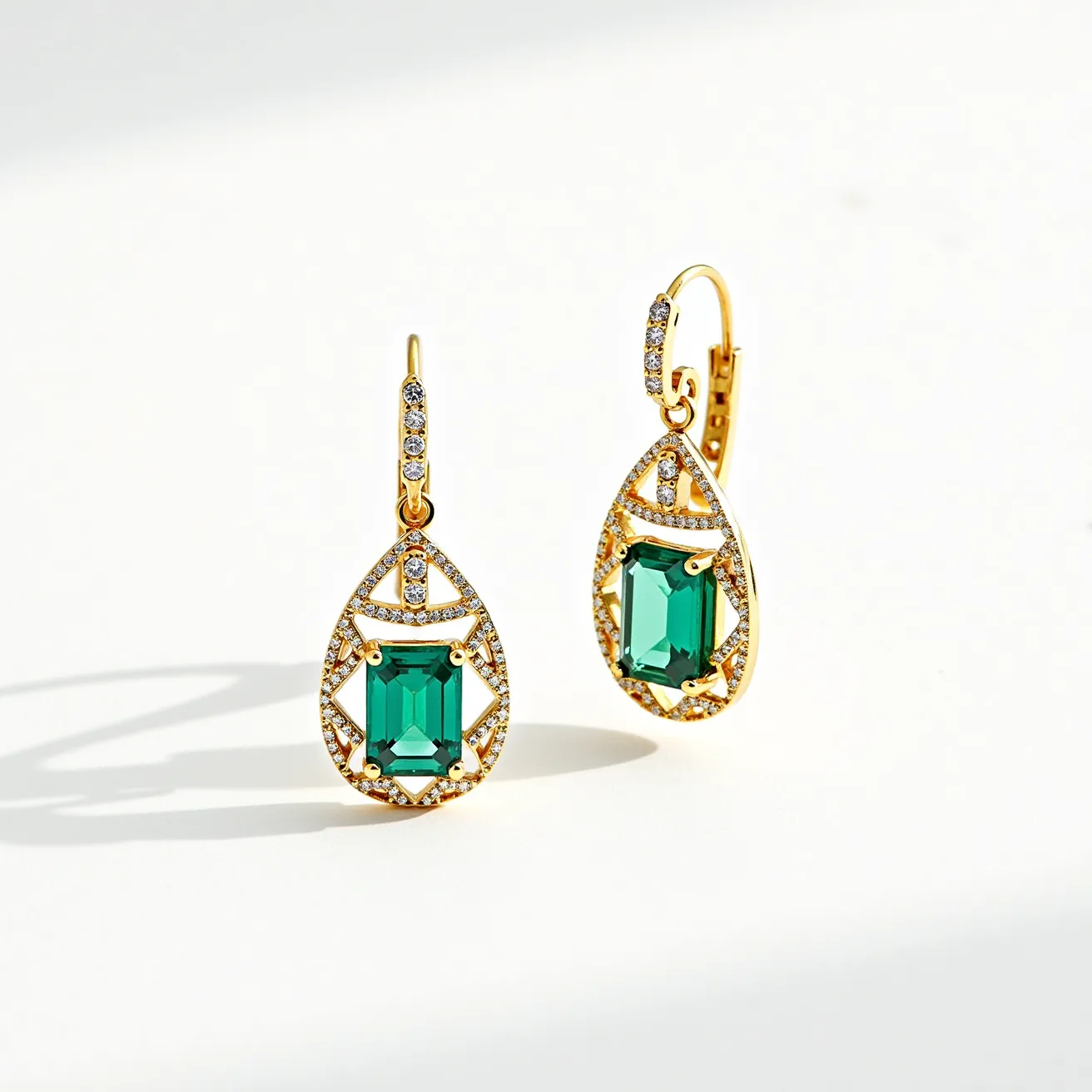 These gold teardrop earrings showcase an elegant design featuring an emerald-cut green gemstone as the central focal point. Each earring is adorned with smaller clear stones accentuating the outer edge of the teardrop shape, creating a sparkling frame. The green gemstone is securely held in place by four prongs, allowing for maximum light reflection and brilliance. Attached with a lever-back clasp, the earrings offer a secure and comfortable fit. The combination of gold and green, along with the intricate detailing of smaller stones, lends a sophisticated and timeless appeal to these earrings.