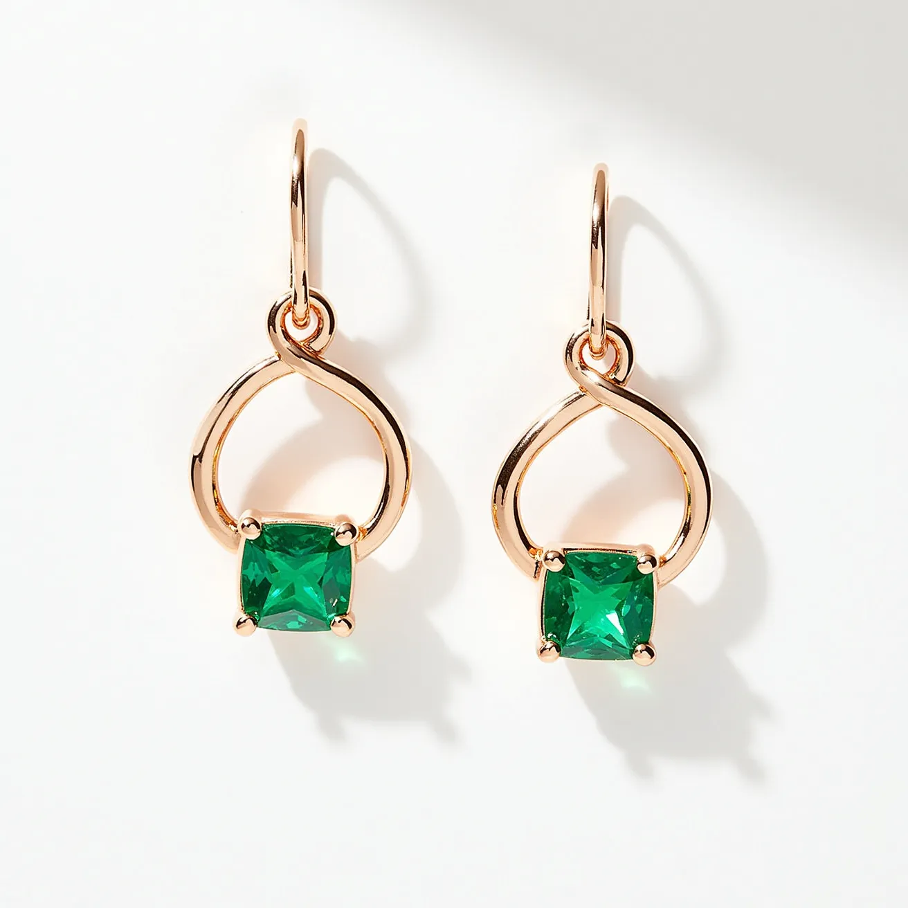 These gold teardrop earrings feature a sleek and elegant design crafted from polished gold. At the heart of each earring is a striking square-cut green gemstone, securely held in place by a four-prong setting. The teardrop shape elegantly frames the gemstone, adding a touch of sophistication and contrast to the vivid green stone. These earrings use a simple hook clasp, allowing them to dangle gracefully and capture the light with every movement. The combination of the gold teardrop and the vibrant green stones creates an exquisite piece of jewelry that exudes charm and elegance.