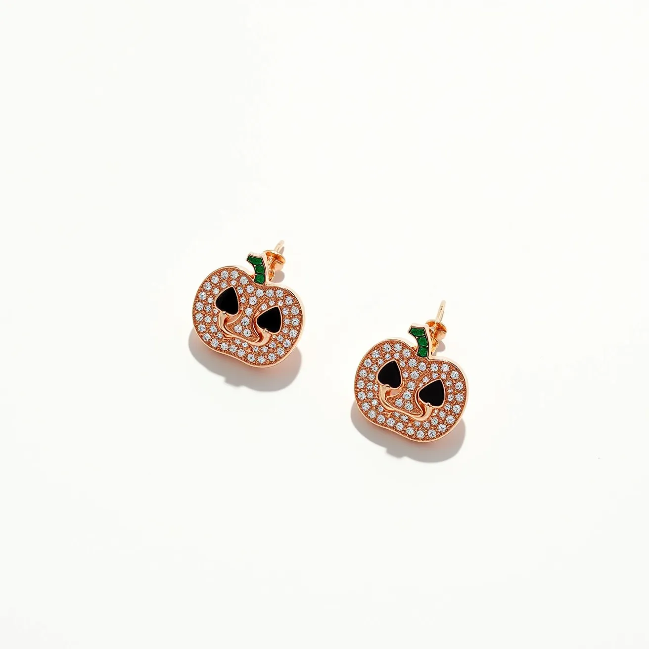 These Halloween earrings feature a playful pumpkin design crafted from a gold-toned metal. The pumpkin faces are accented with numerous small, clear stones that appear to be set in a pavé style, adding a sparkling texture to the surface. Black enamel forms the eyes and mouth, enhancing the jack-o'-lantern look. At the top, there is a small green stem inset with a single green stone, adding contrast to the overall design. The earrings are secured with a typical post and butterfly clutch back, ensuring they stay comfortably in place when worn.