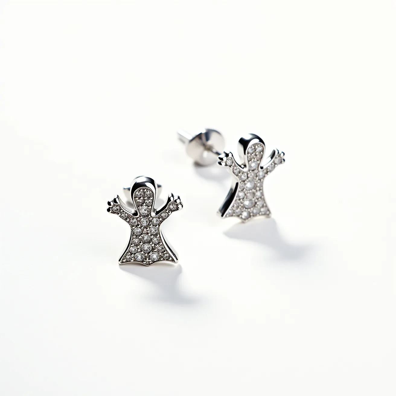 These halloween earrings feature a playful ghost design, crafted from a polished metal likely to be a silver-tone or white gold, providing a sleek and shiny finish. Each earring is studded with numerous small, clear gemstones, possibly cubic zirconia or diamonds, that are pavé set to create a sparkling surface. The uniformity and arrangement of these stones add a textured brilliance to the ghost's form. The earrings are designed with a stud post and a butterfly back clasp, offering secure and comfortable wear. These elements together form a charming accessory that captures the festive and whimsical spirit of Halloween.