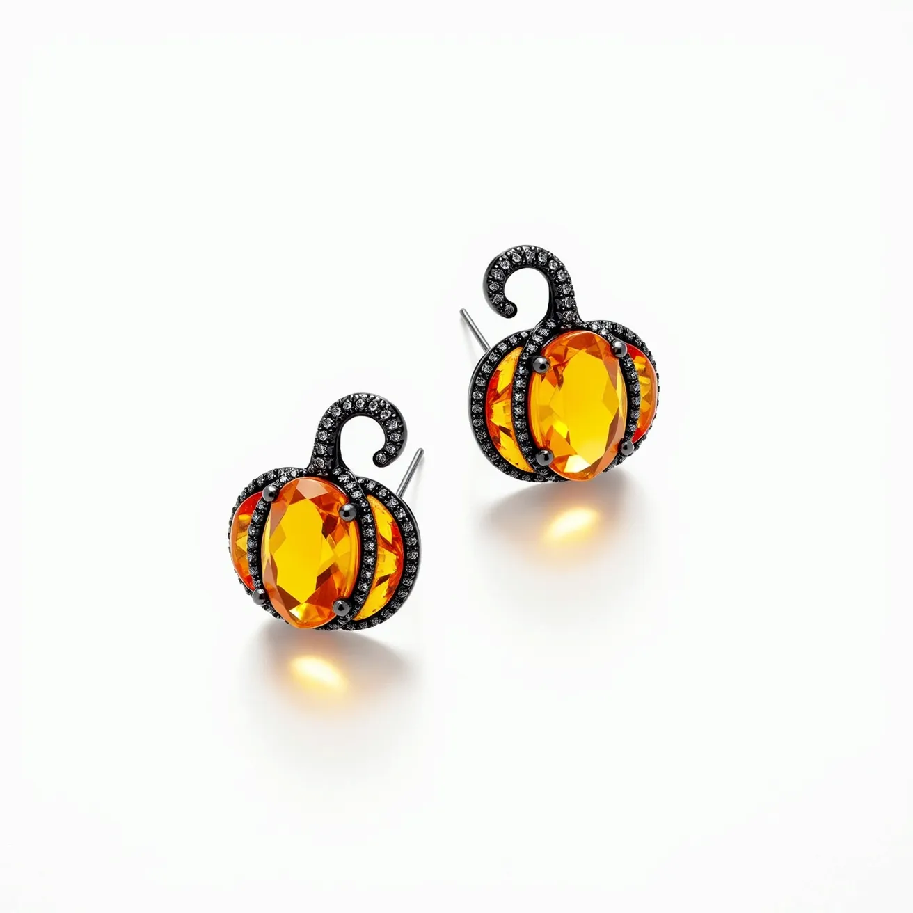 These Halloween earrings feature a playful pumpkin design, highlighting a central orange gem with an oval cut, giving the appearance of a carved pumpkin. The gem is set securely with multiple prongs, surrounded by a band of smaller black stones that create a glimmering contrast. The metallic structure holding the stones showcases a textured finish, further enhancing the thematic detailing. Each earring is equipped with a standard post and push-back clasp, ensuring a secure and comfortable fit.