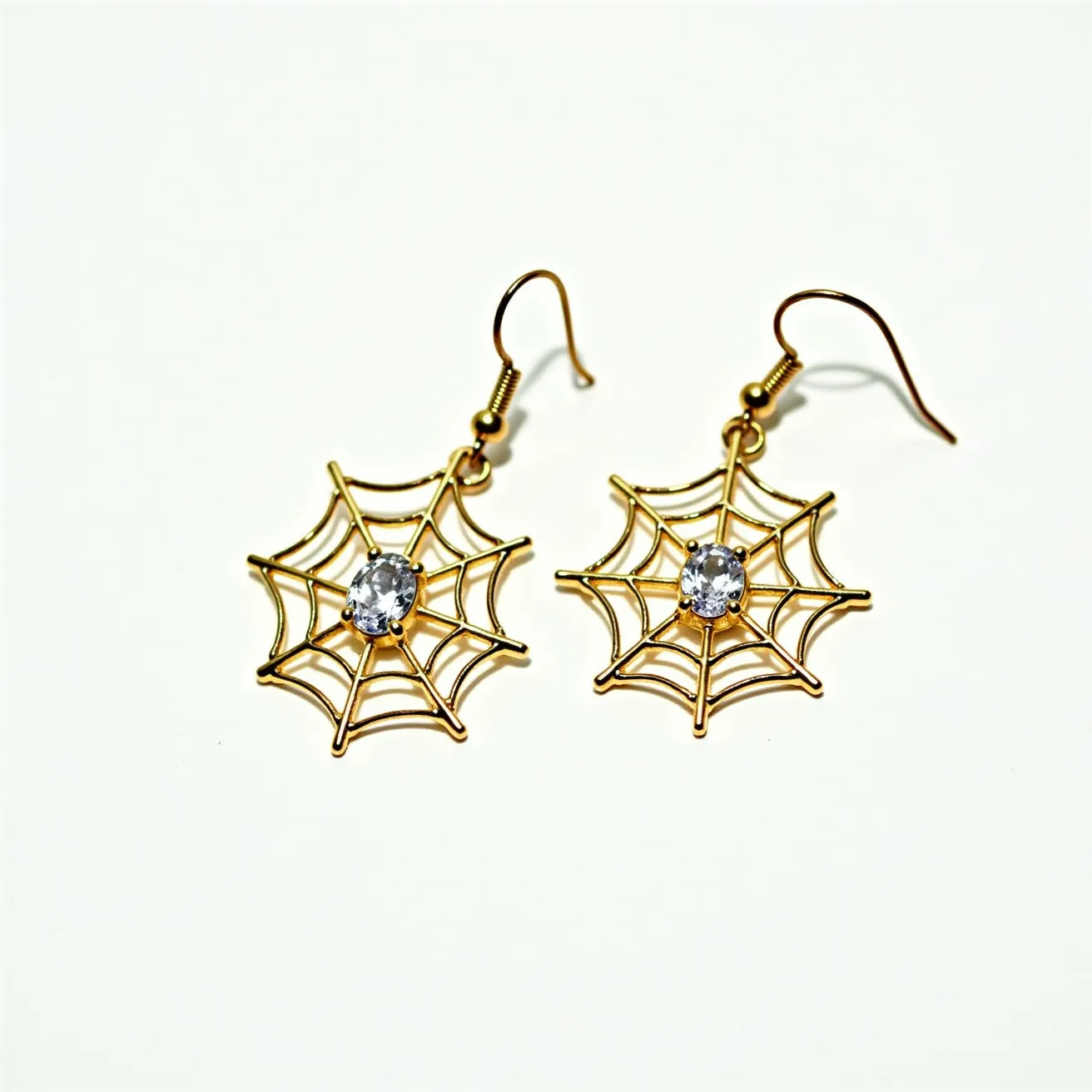 These Halloween earrings feature a delicate spider web design crafted from a gold-colored metal. Each earring showcases a central, round, faceted gemstone, likely a clear crystal or rhinestone, set in a simple prong setting that adds a touch of sparkle. The intricate web design is suspended from a hook-style clasp, providing ease of wear and a secure fit. The overall aesthetic combines festive Halloween elements with a touch of elegance, making these earrings a charming accessory for the season.