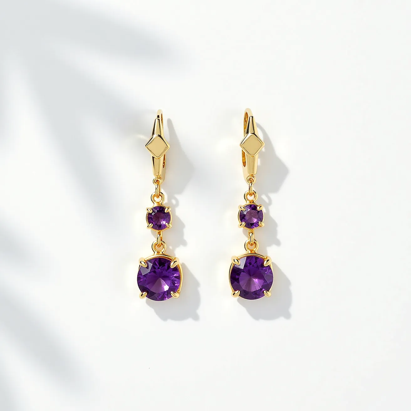 These hanging earrings feature a striking combination of gold-tone metal and vibrant amethyst gemstones. Each earring boasts two round-cut amethysts; the smaller gem is positioned above the larger one, creating a balanced and elegant drop. The stones are set in a classic prong setting, which highlights their rich purple color and faceted design, enhancing their sparkle. The earrings are completed with lever-back clasps, ensuring a secure and comfortable fit while adding a stylish geometric touch to the overall design.