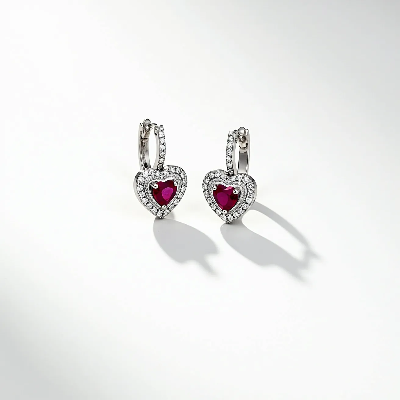 These heart diamond earrings feature a combination of precious metals and stones. The design centers around heart-shaped rubies, which are surrounded by a halo of small, round-cut diamonds that enhance their brilliance. The diamonds are set in a white metal, possibly white gold or platinum, commonly used to provide a secure and elegant setting. The earrings are attached with a hinged hoop clasp that securely fastens them to the wearer’s ears, offering both style and comfort. The combination of the red rubies with the sparkling diamonds creates a striking contrast, making these earrings an exquisite piece of jewelry.