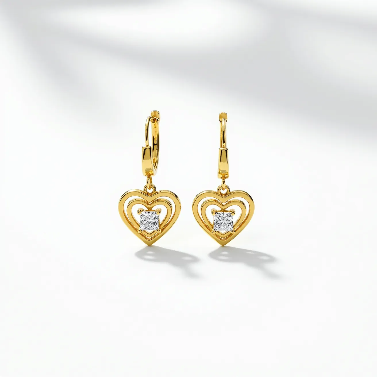 These heart earrings set features a delicate design crafted from a polished gold-tone material, creating an elegant framework for each earring. At the center of each heart is a square-cut gemstone, likely a diamond or diamond simulant, set in a secure prong setting that accentuates its brilliance. The earrings attach with lever-back clasps, ensuring both security and comfort for the wearer. The open-heart design combined with the sparkle of the central stone gives these earrings a timeless and romantic appeal.