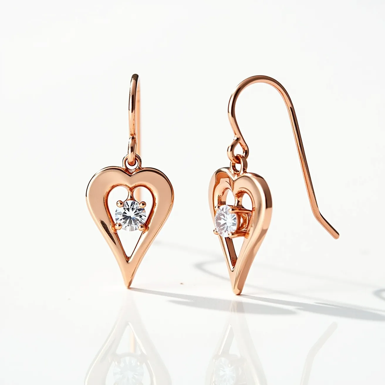 These heart earrings feature a delicate open-heart design crafted from a polished rose gold-tone metal. At the center of each heart is a sparkling gemstone, likely a round-cut cubic zirconia, securely held in place by a classic four-prong setting, adding a touch of elegance and brilliance. The earrings are designed with a simple hook clasp, allowing for easy and comfortable wear. The combination of the metallic shine and the clear sparkle of the gemstones creates a timeless and chic accessory.