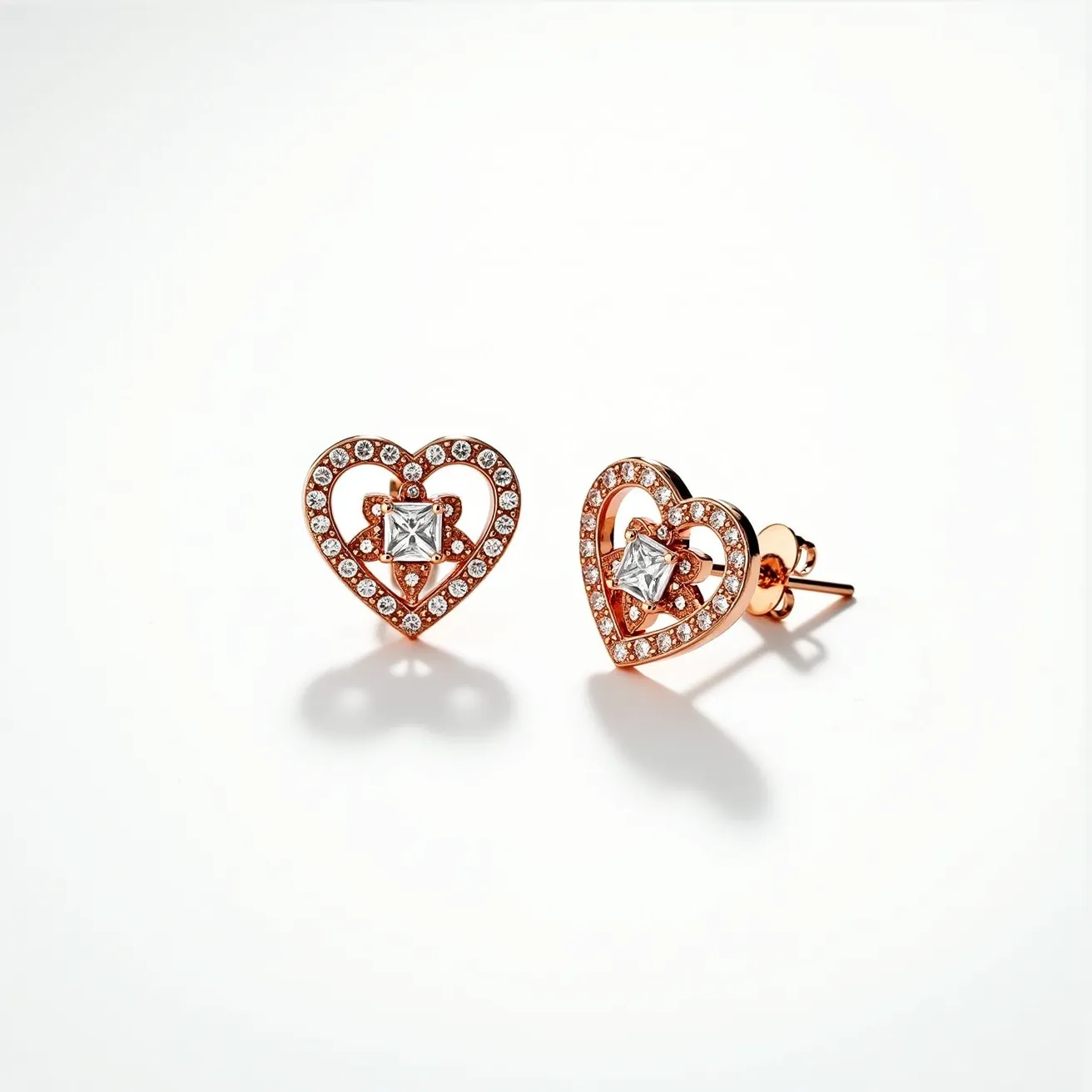 These heart earrings showcase a delicate design with rose gold metal forming the shape of a heart. Each earring is adorned with a halo of small, round, clear stones, likely diamonds, that are pave set to accentuate the heart shape. At the center, a prominent square-cut gem, possibly a diamond or a cubic zirconia, is securely set in a prong setting, adding a striking focal point to the piece. The earrings are attached with a classic post and butterfly back clasp, ensuring both security and style.